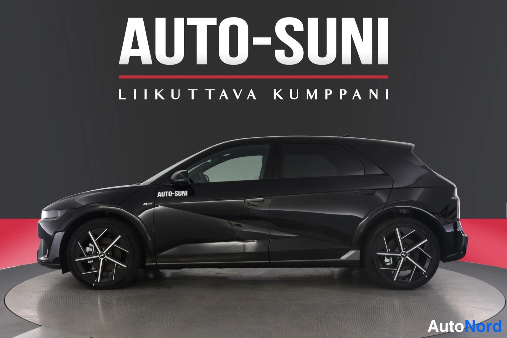 Sivulta: Tummansävyinen Hyundai IONIQ 5 sivuprofiilista studiotaustaa vasten, Auto-Suni-logo kuvan yläosassa.