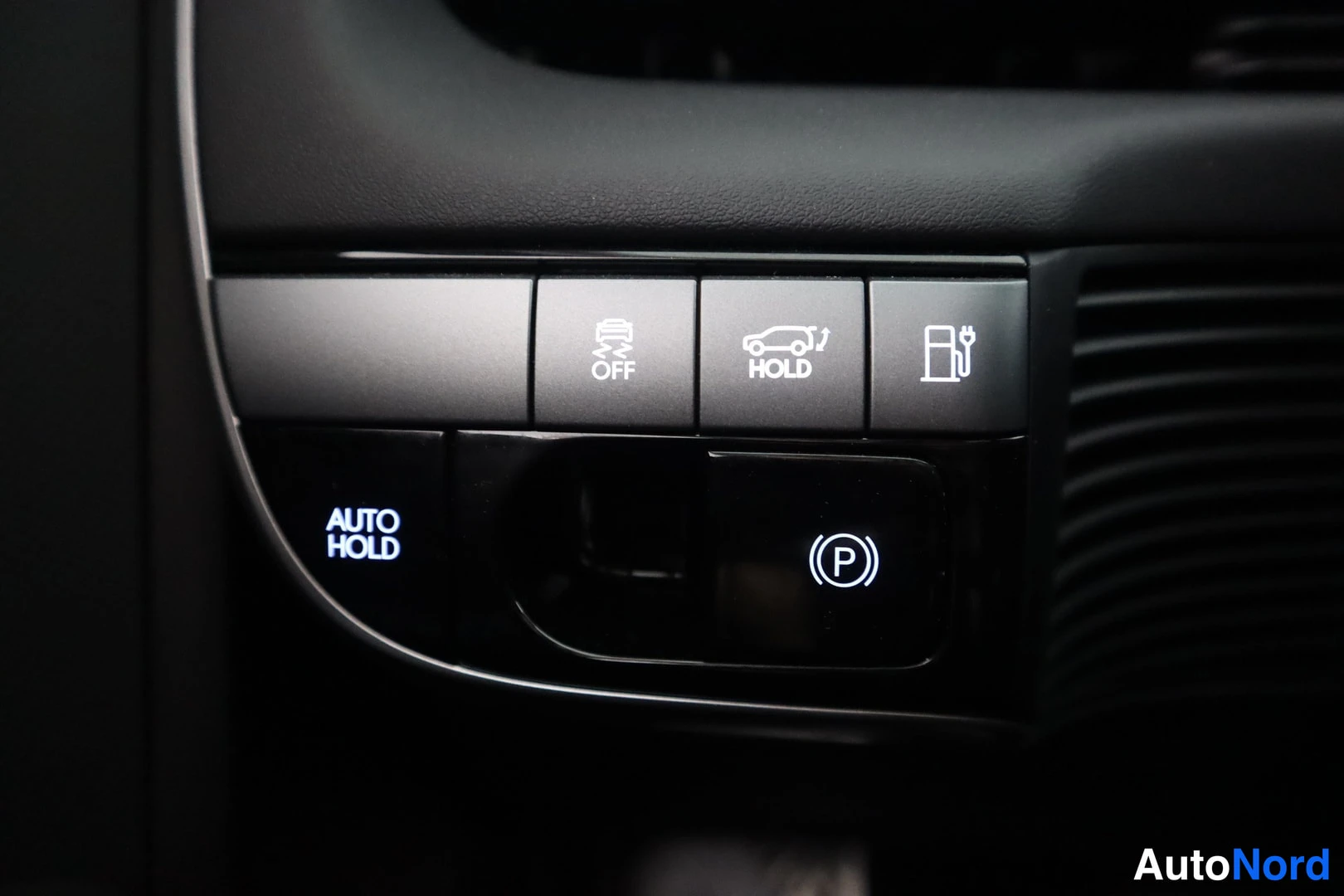 Sivulta: Keskikonsolin painikepaneeli, jossa sähköinen parkkijarru (P), AUTO HOLD, liukuesteen OFF- ja HOLD-painikkeet sekä latausportin symboli.