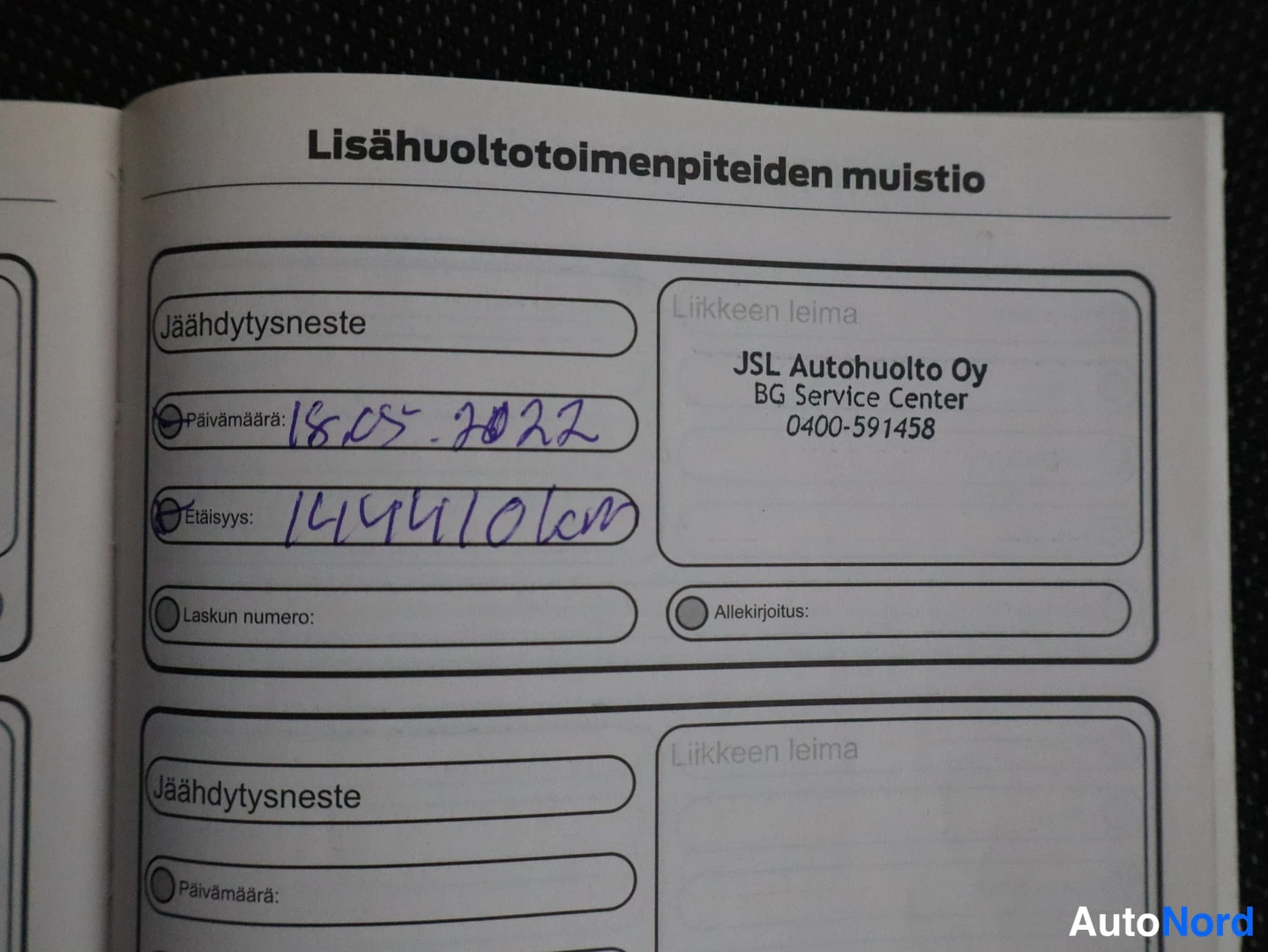 Asiakirja: Huoltokirjan sivun lähikuva, Lisähuoltotoimenpiteiden muistio -osiossa käsinkirjoitettu jäähdytysnesteen vaihto 18.05.2022, 144410 km.