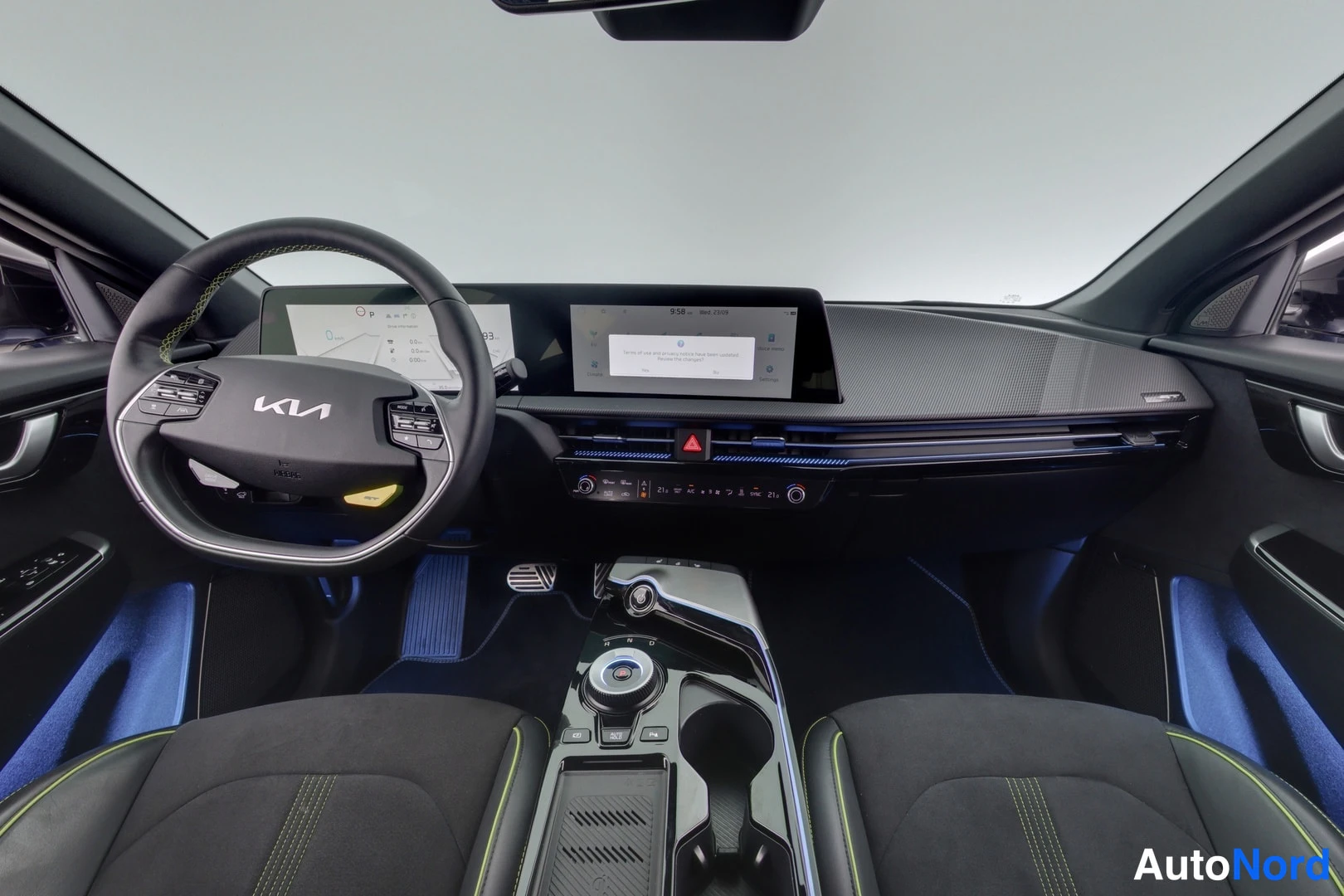 Yksityiskohta: Kia EV6:n kojelauta ja ohjauspyörä, kaksiosainen leveä näyttö, sininen Kia-merkki ohjauspyörässä ja huomioliivi aukiostossa.