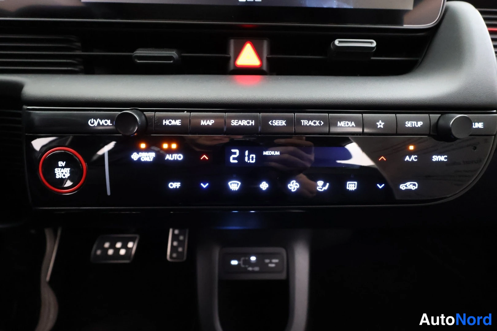 Yksityiskohta: Keskikonsolin lähikuva: infotainment-napit (HOME, MAP, SEARCH, MEDIA, SETUP), ilmastointipaneeli näyttää 21,0 ja A/C sekä EV START STOP -painike punaisella kehy