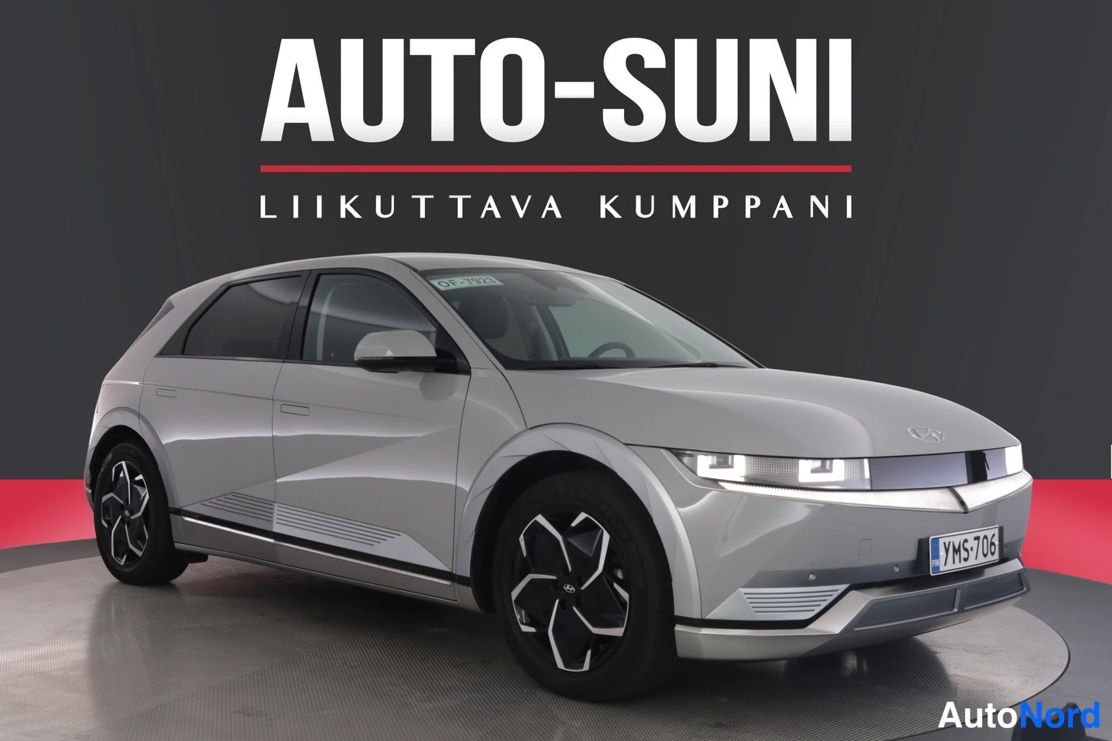 Etuviisto, nokka oikealle: Autosuni-logo tummalla taustalla; hopeanharmaan Hyundai IONIQ 5:n etukulmanäkymä kulmikkailla LED-ajovaloilla ja neliosaisilla kevytmetallivanteilla. Rek