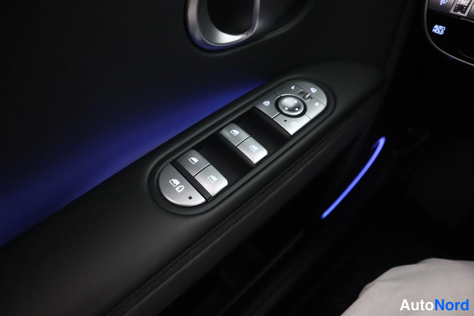 Muu: Oven sisäpaneeli: ikkunoiden ja peilien säätönapit, sininen tunnelmavalo ja osittain näkyvä AUTO HOLD -nappi.