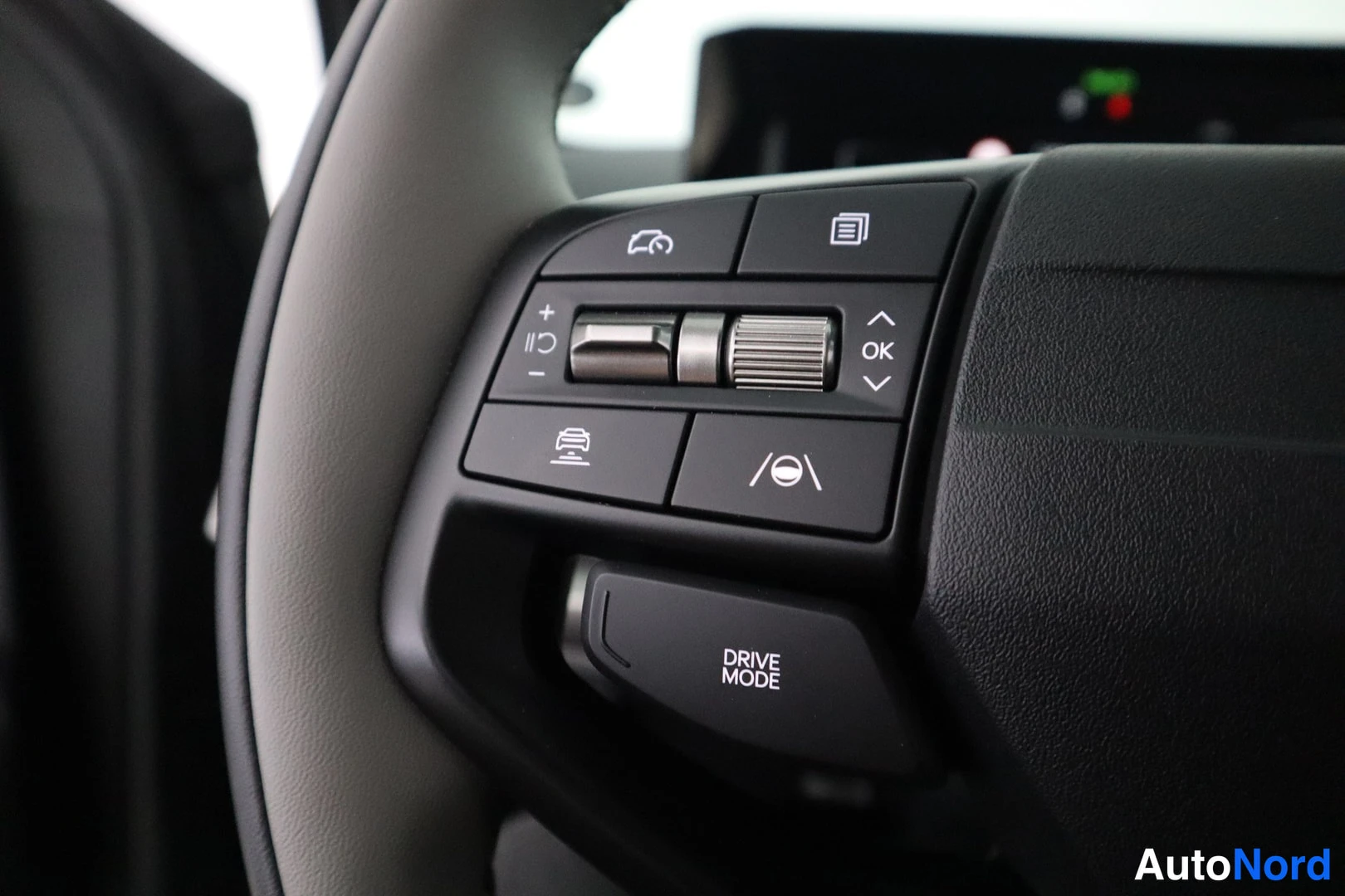 Yksityiskohta: Ohjauspyörän vasen puhelinke itäinen ohjainpaneeli, jolla on merkit kuten OK, risteilevät nuolet ja DRIVE MODE.