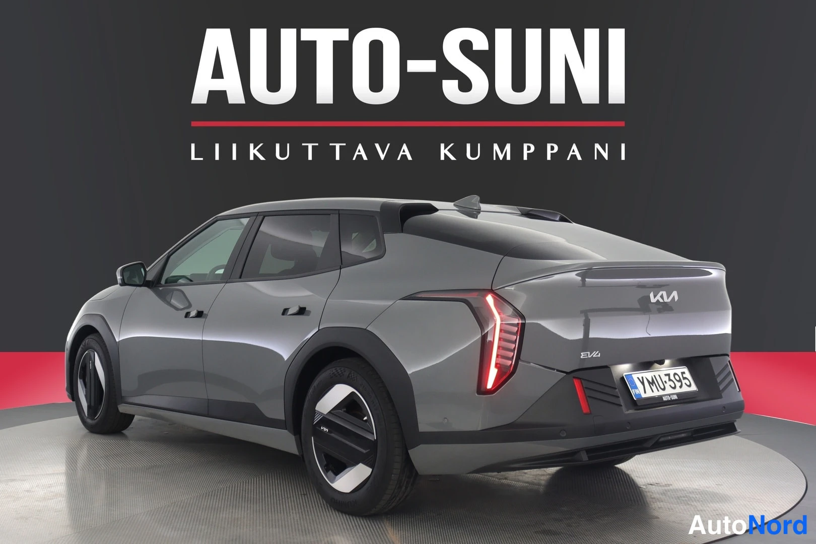 Takaviisto: Kia EV4, takaosa kolmesta neljäsosasta näkyvissä vasemmalta, harmaa koripaneeli, takavalo ja rekisterikilpi YMÜ-395