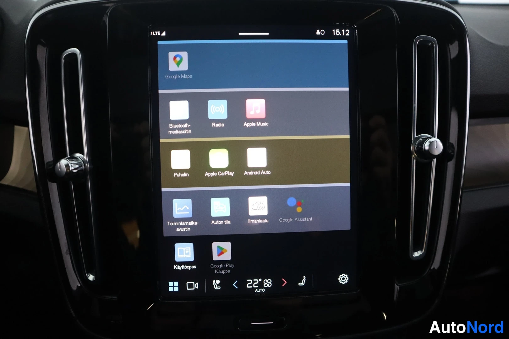 Yksityiskohta: Auton keskikonsolin infotainment-näyttö pystyasennossa, jossa näkyy sovellusvalikko: Google Maps, Radio, Apple Music, Puhelin, Apple CarPlay, Android Auto, Goog