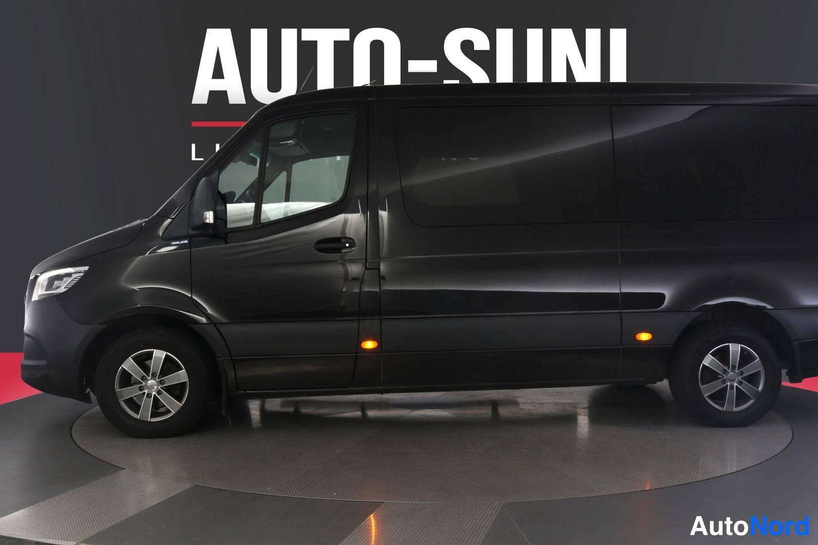 Sivulta: Mustan Mercedes-Benz Sprinter -pakettiauton kylki suoraan sivulta kuvattuna studioympäristössä, pyörät ja ovet näkyvissä.