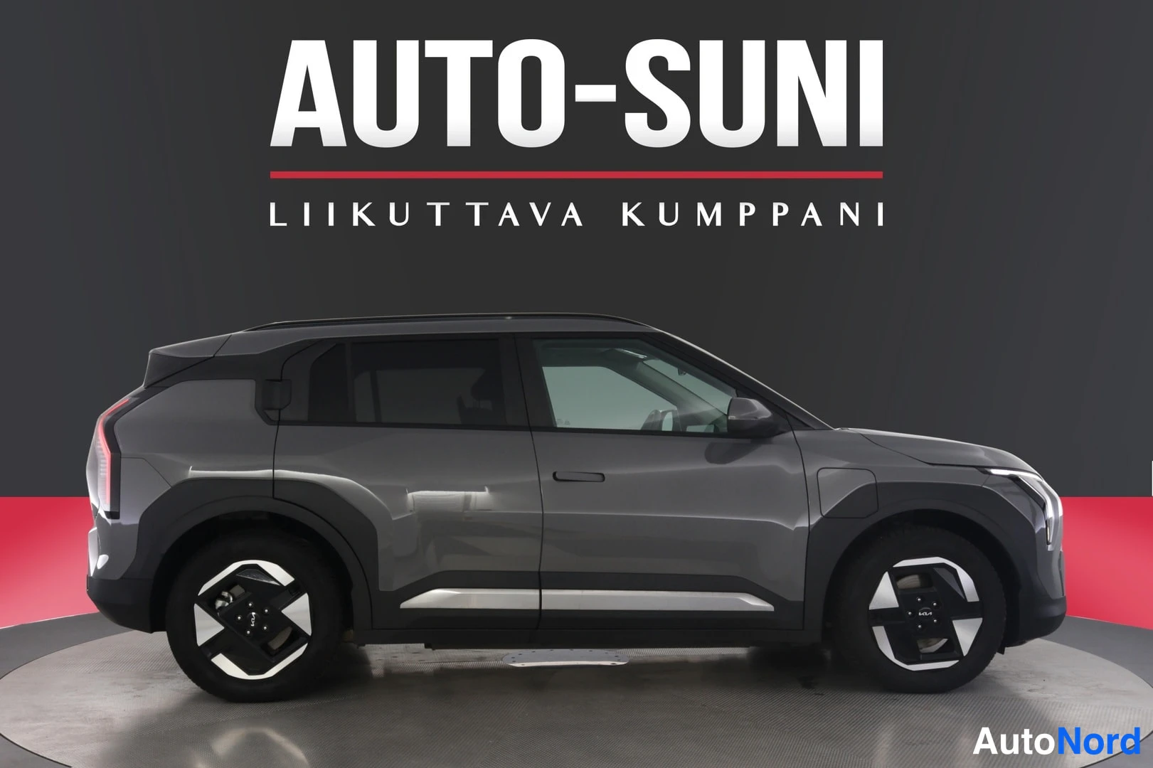 Sivulta: Auton sivuprofiili valokuvausstudiossa, harmaa Kia EV3, AUTO-SUNI-logo taustalla.