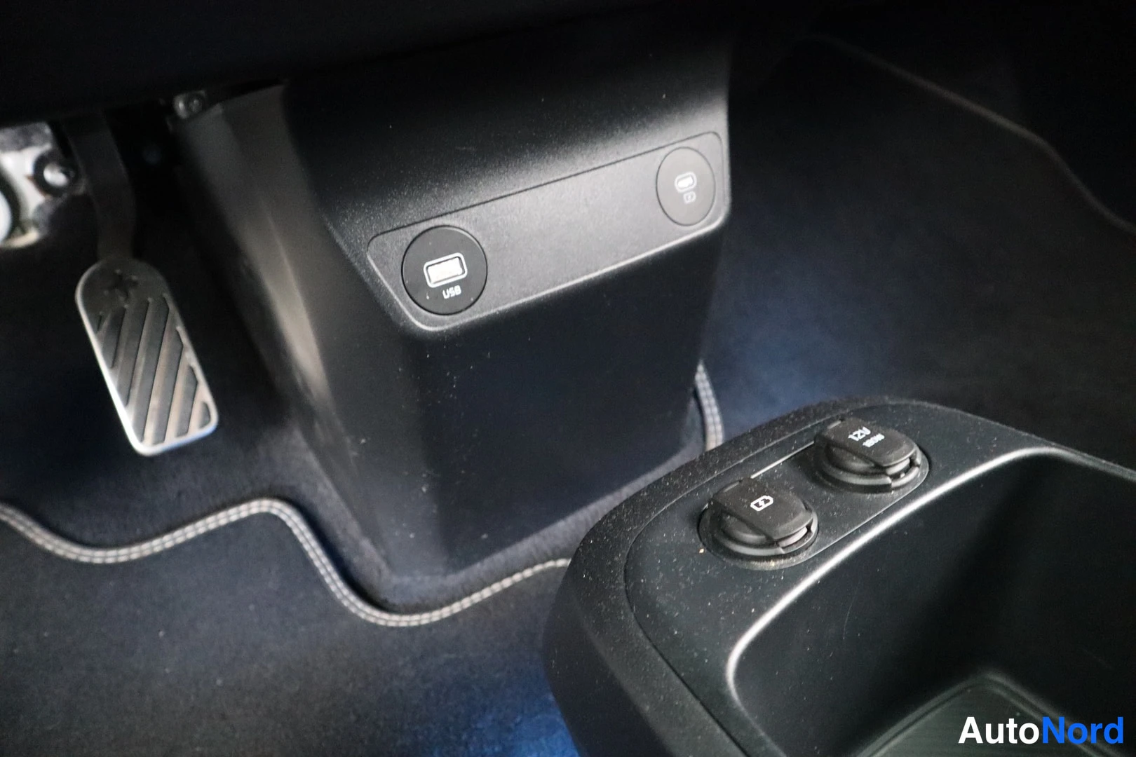 Muu: Ohjaamon alusta: USB-portti ja 12V-pistorasia keskikonsolin etuosassa, poljintiloan metallinen kaasupoljin ja tummat mattot.