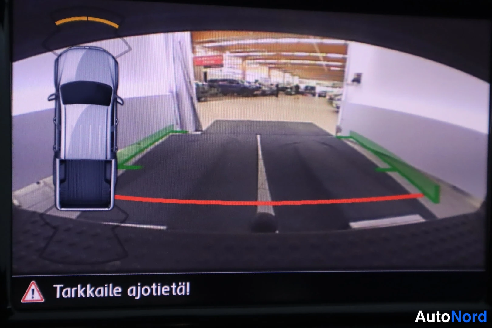 Yksityiskohta: Takakamerakuva näyttöruudulla. Takajärjestelmä esittää autosta ylhäältä katsottuna siluetin ja viiva-ohjeistuksen parkkeeraamiseen. Punainen ja vihreät viivat i