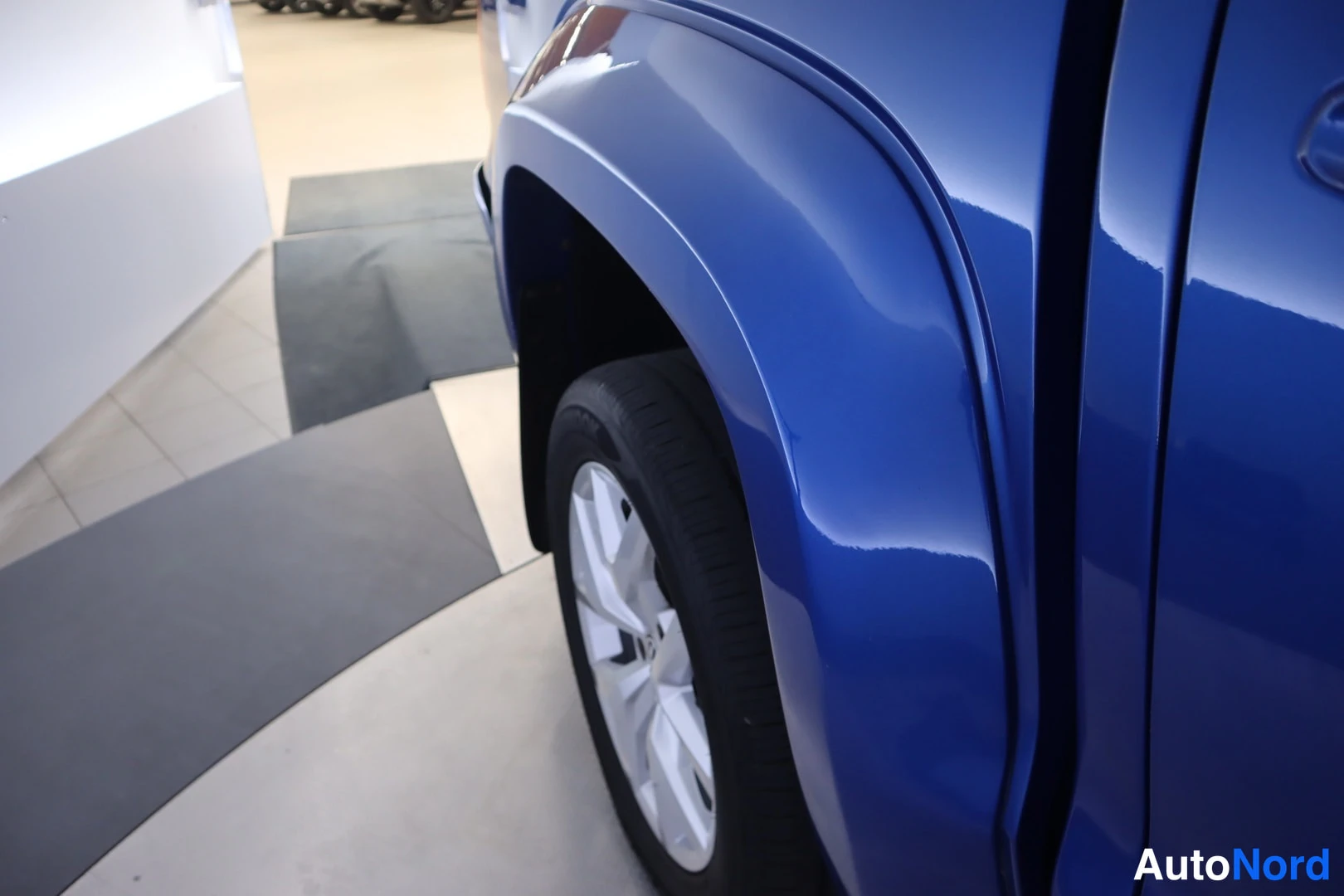 Sivulta: Lähikuva auton sinisestä etufenderistä ja etupyörästä hopeavanteella.