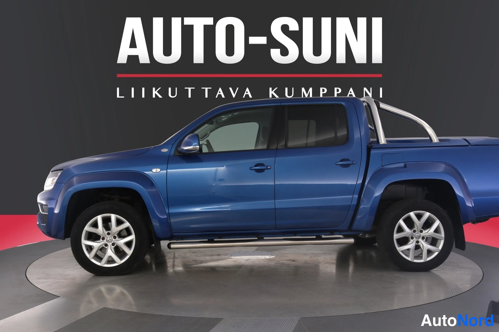Sivulta: Blue dual-cab pickup truck shown from the driver-side profile view. It has silver alloy wheels and a chrome side step.