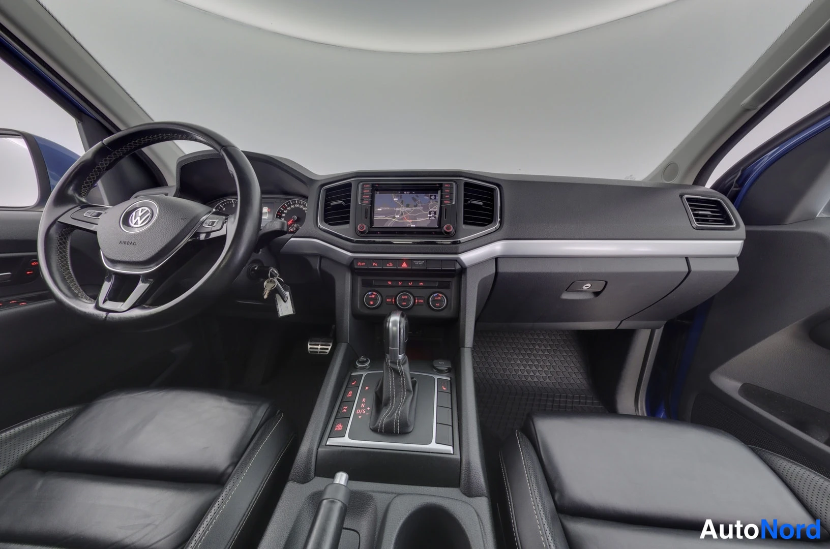 Ohjaamo: Dashboard and center console interior showing leather-wrapped steering wheel, infotainment screen with navigation map, gear selector, and climate controls.