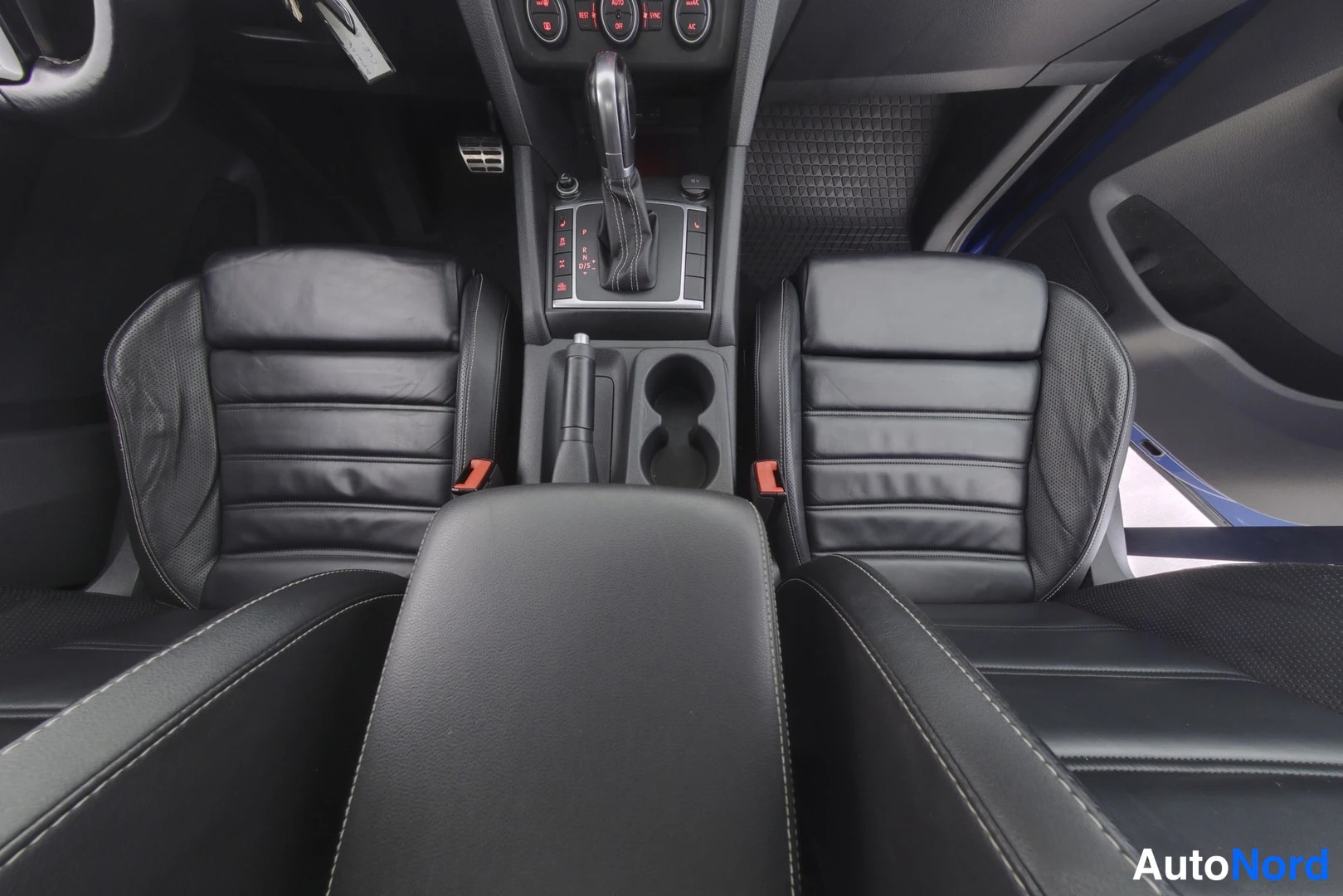 Etuistuimet: Black leather front seats of a vehicle with visible center console featuring automatic gear shifter and cupholders. The shot is taken from the perspective behin