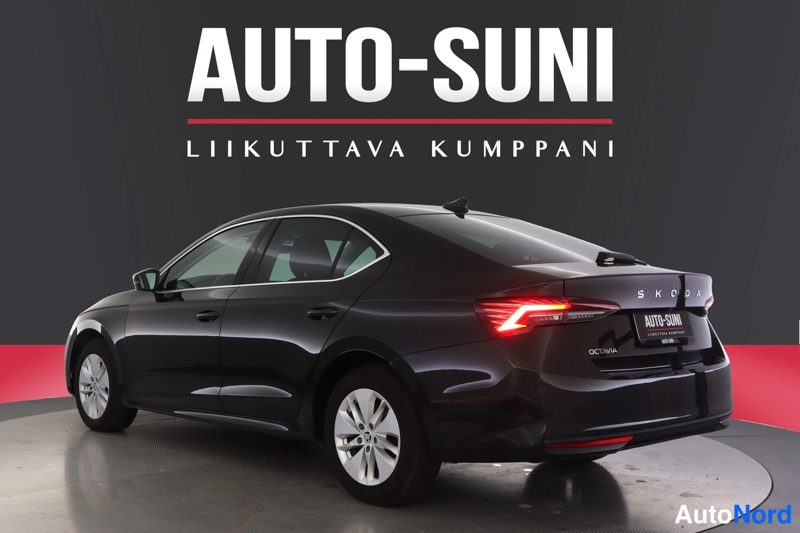 Takaviisto: Takakulmasta kuvattu tumma henkilöauto: peräluukussa lukee ŠKODA ja OCTAVIA, takavalot ovat päällä ja auton vasen kylki ovineen sekä pyörät näkyvät kuvassa.