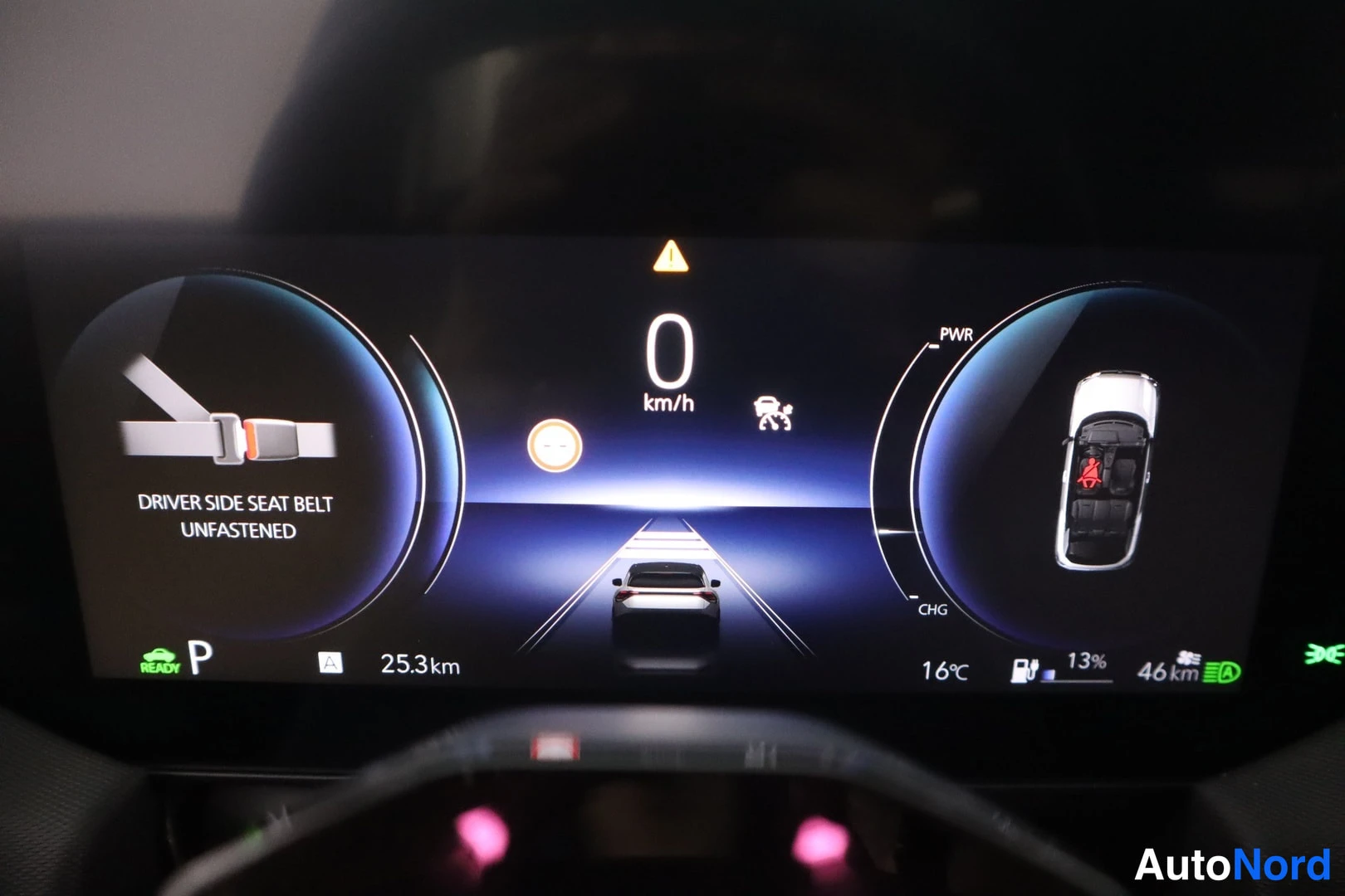 Yksityiskohta: Digitaalinen kojetaulunäyttö: nopeus 0 km/h, vaihde P ja READY-merkintä, vasemmalla varoitus 'DRIVER SIDE SEAT BELT UNFASTENED', alareunassa 25.3 km, 16 °C, 13