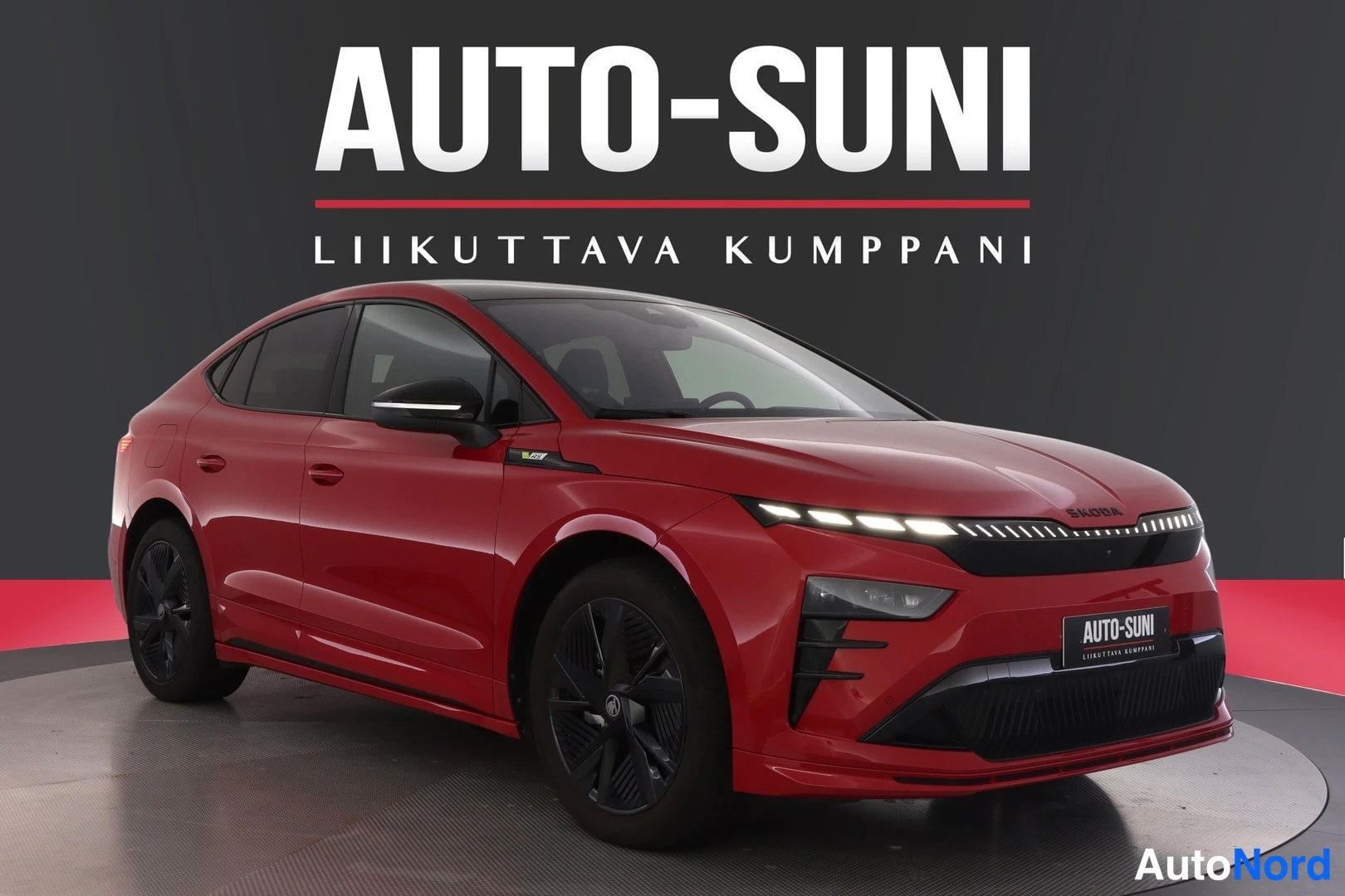 Etuviisto, nokka oikealle: Front three-quarter view of a red Skoda SUV in a studio with the front grille and driver's side visible.