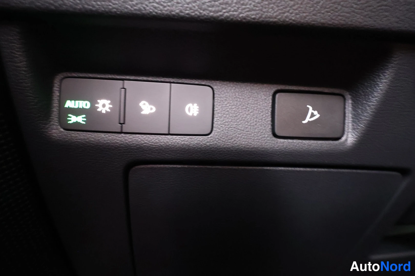 Yksityiskohta: Close-up of illuminated switch panel including AUTO headlight button, fog light symbol, and traction control off button