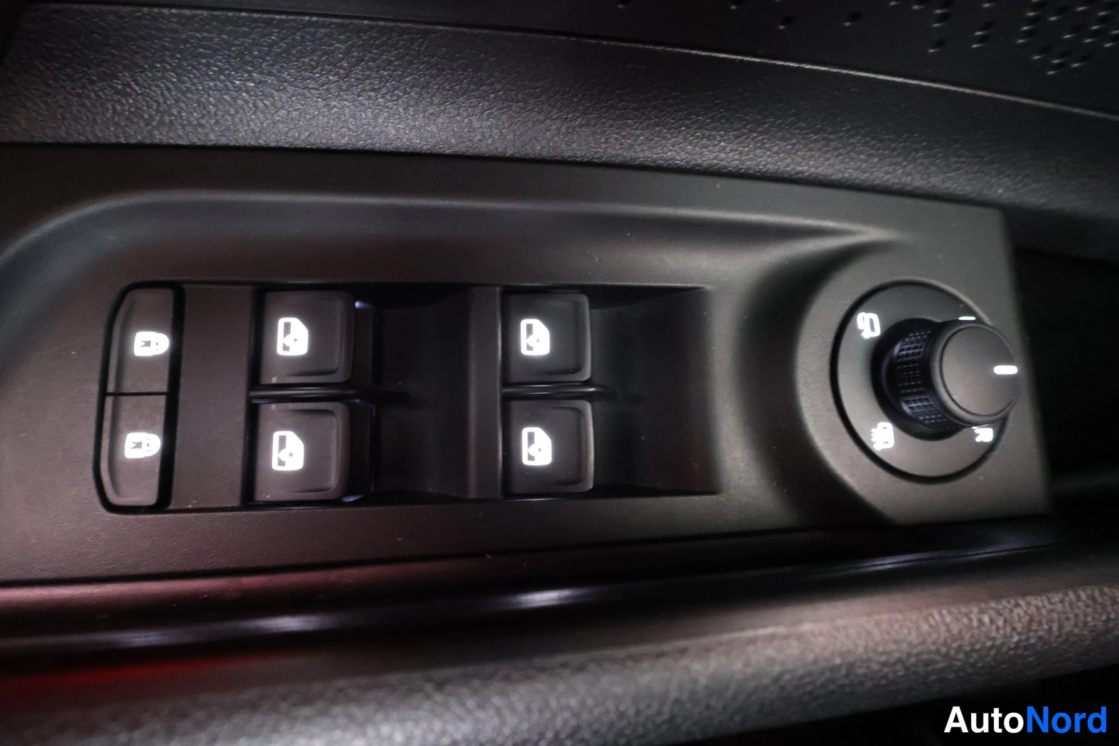 Yksityiskohta: Door control panel with four illuminated electric window buttons on the driver side and a headlight knob