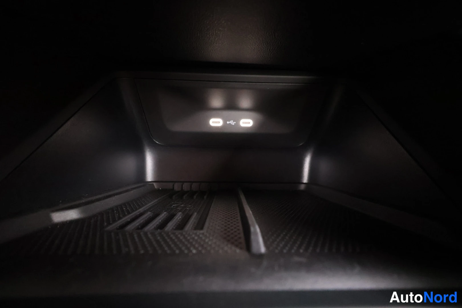 Tavaratila: Storage console area containing two white USB ports, located below an air vent slot