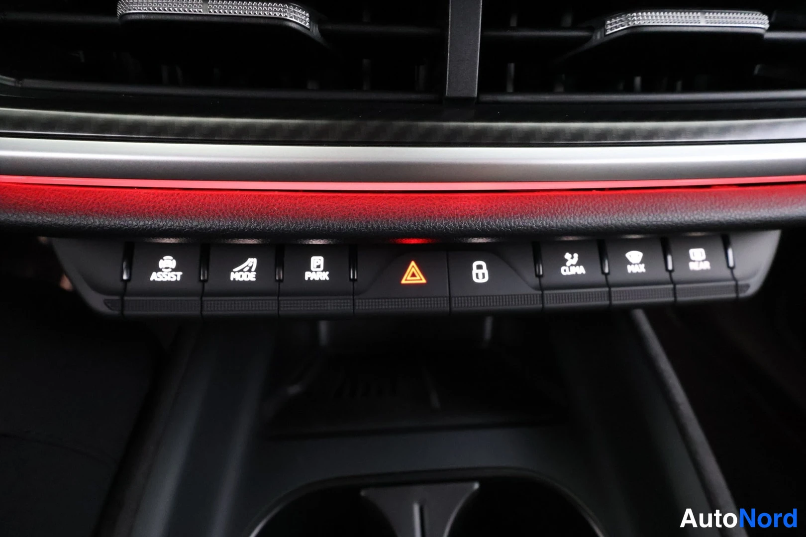 Yksityiskohta: Dashboard control row with illuminated hazard warning triangle, lock icon, CLIMA label, PARK label, and REAR label