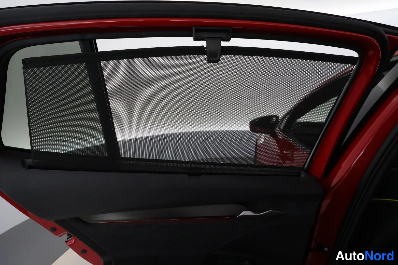 Ohjaamo: Interior view of an open car door frame painted in gloss red. A black mesh sunshade is installed in the window, obscuring the view outside.