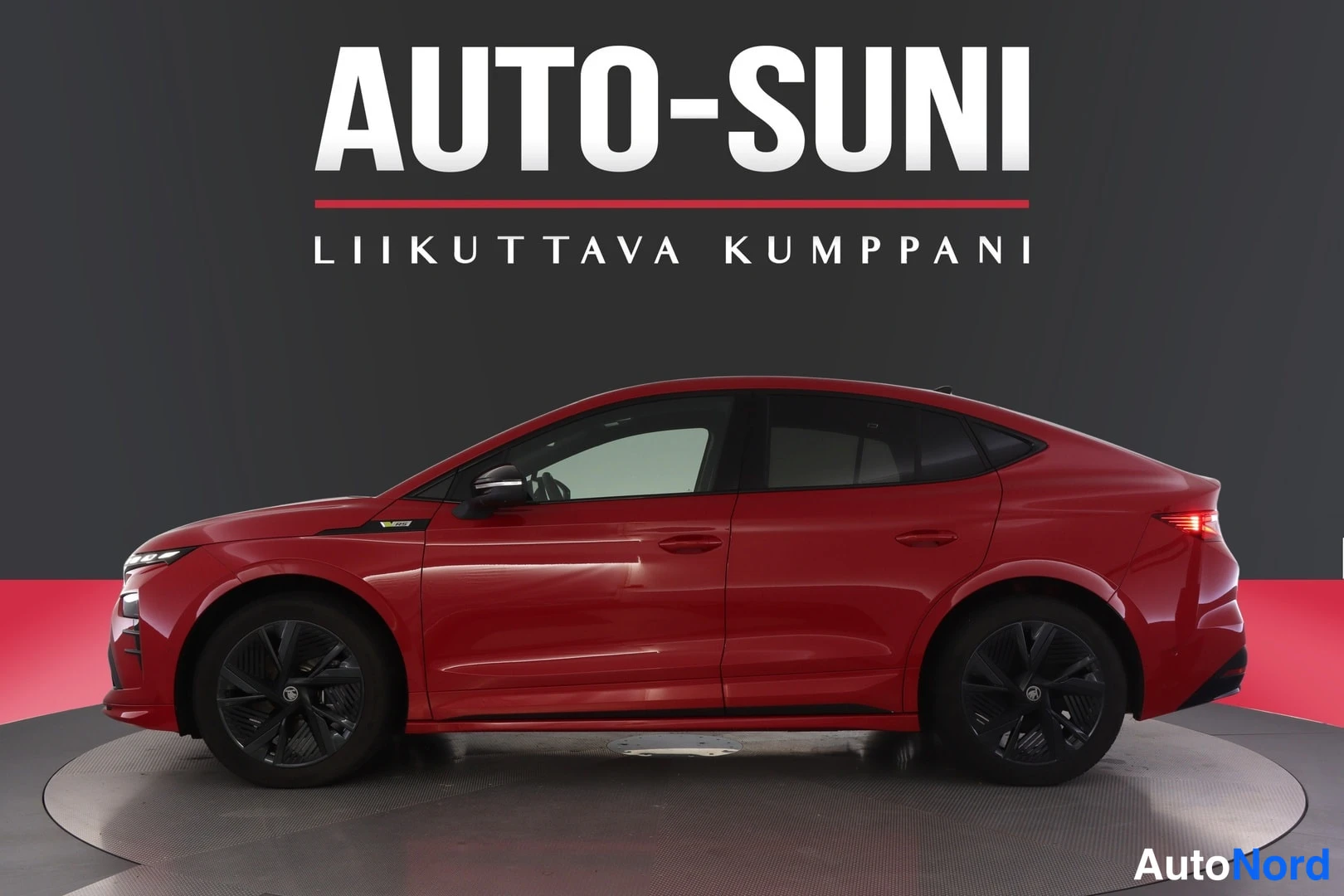 Sivulta: Sivuprofiilikuvassa on koko punainen auto sisätiloissa, valkoisilla vanteilla ja mustalla puskurilla.