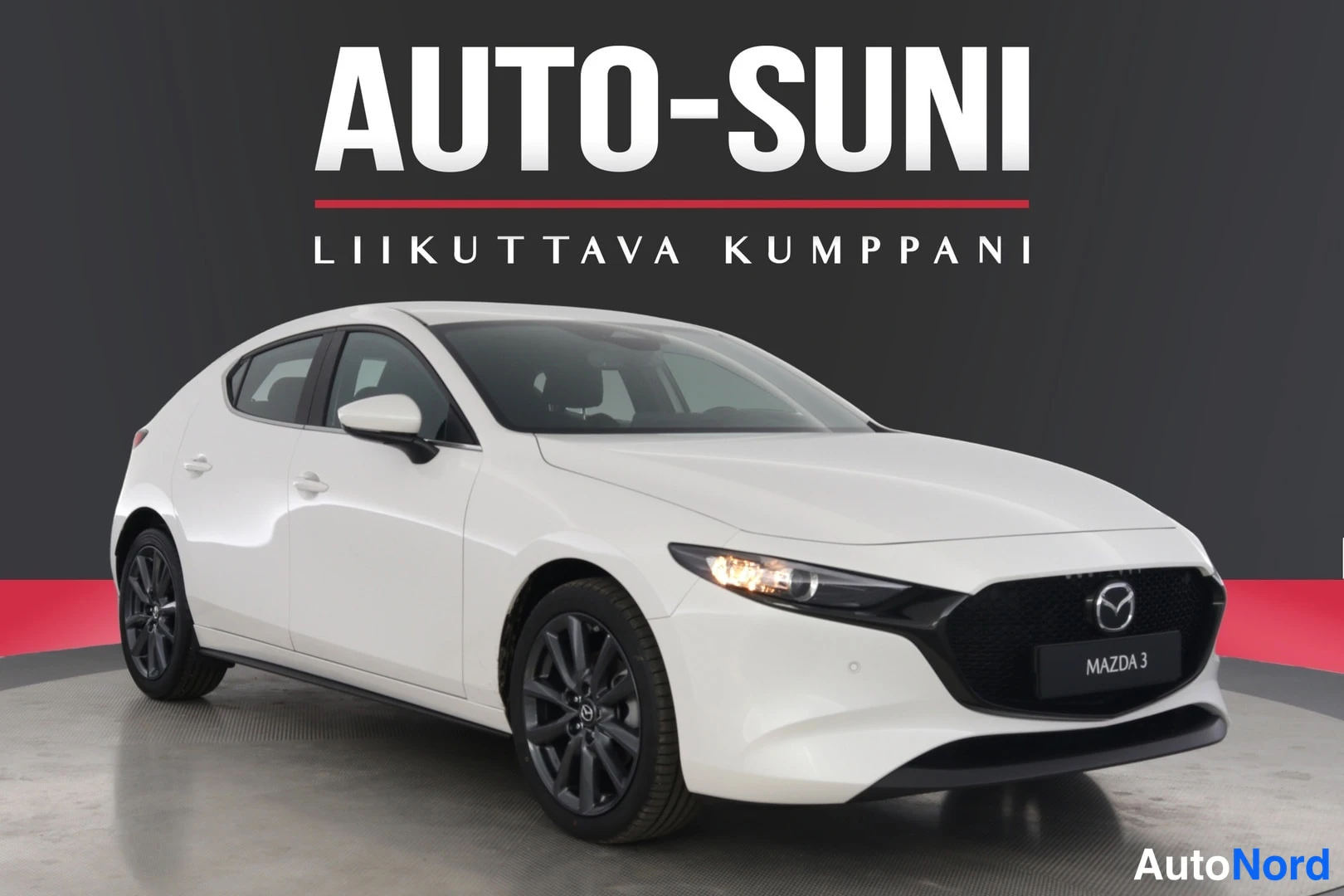 Etuviisto, nokka oikealle: Valkoinen Mazda 3 -viistoperä kuvattu etuviistolta oikealle osoittaen, tummat vanteet jaAuto-Suni-tausta.