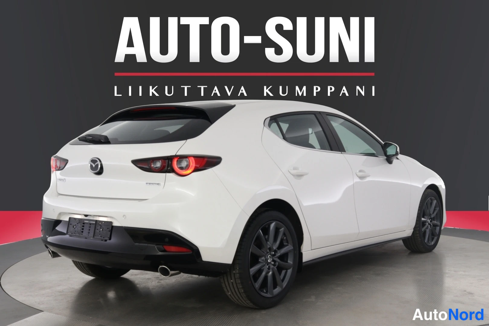 Takaviisto: Valkoinen Mazda 3 takaviistolta vasemmalle, LED-takavalot ja tumma diffelti.