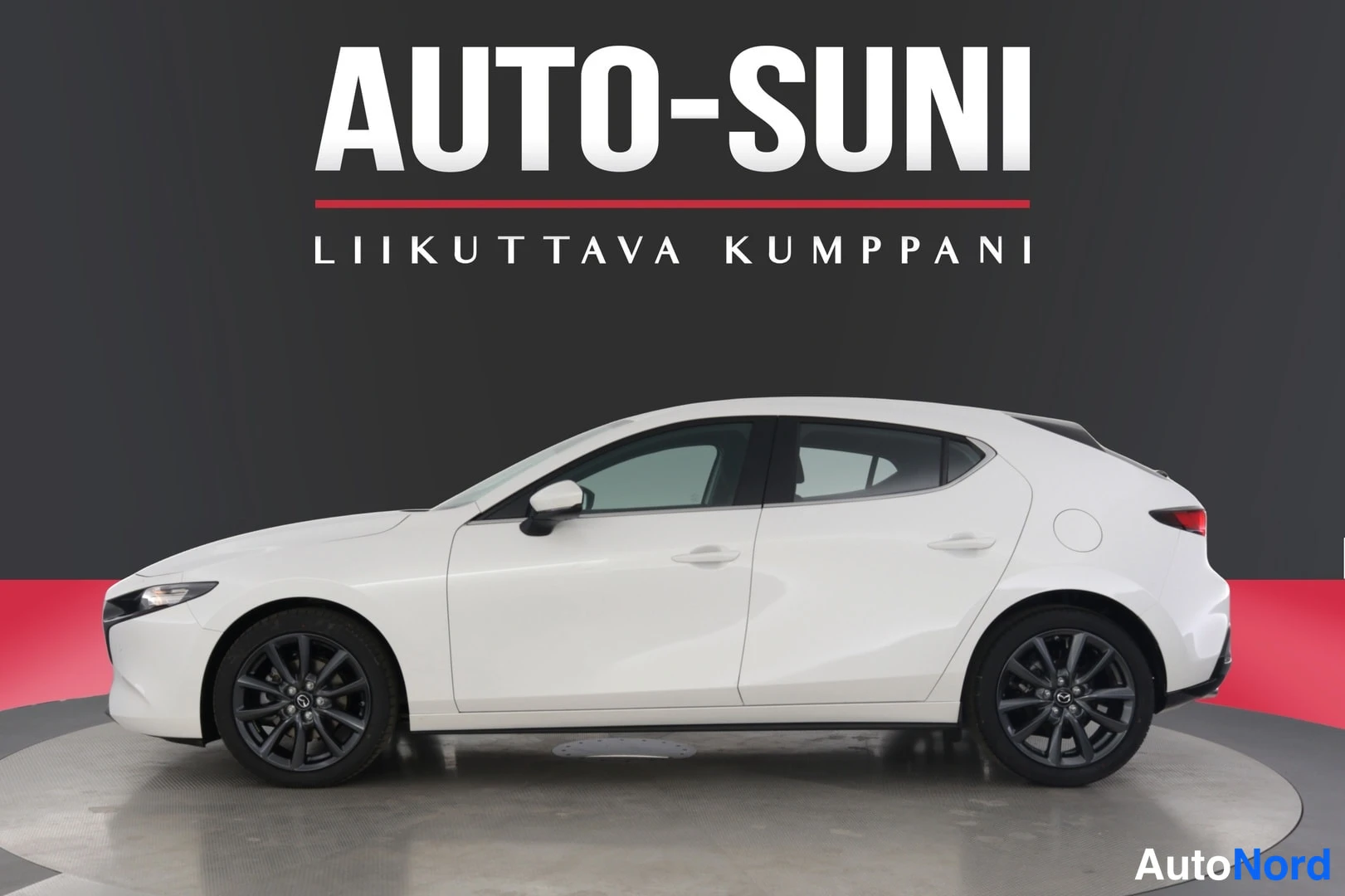 Sivulta: Valkoinen Mazda 3 -viistoperä sivulta kuvattuna studiossa, mustat vanteet ja AUTO-SUNI-logo taustalla.