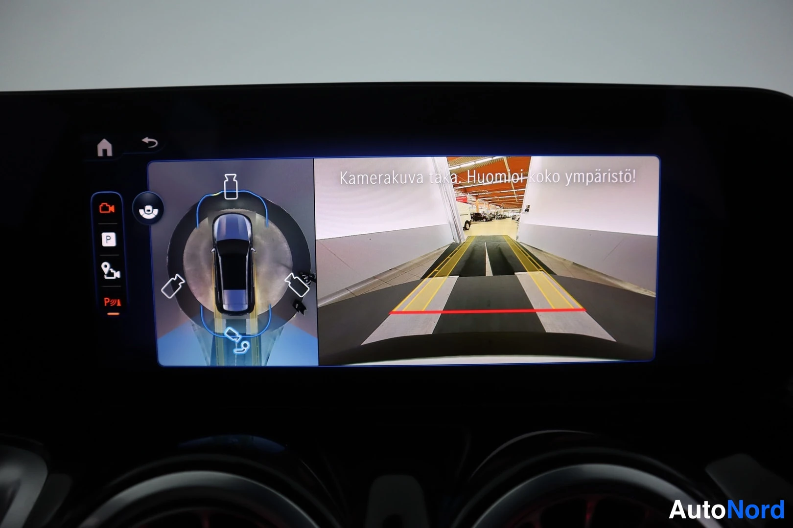 Muu: Istuvan auton infotainment-näyttö näyttää 360-asteisen kamera- ja peruutuskamerakuvan laturihallissa.
