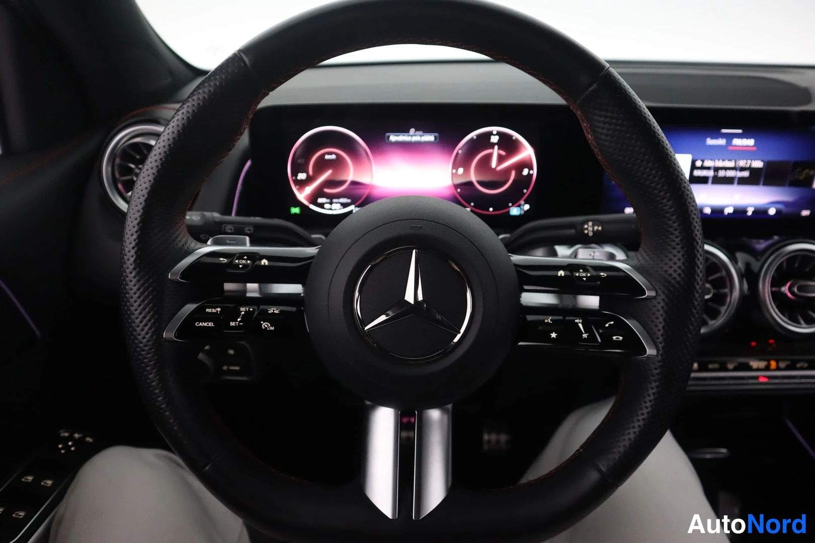 Muu: Mercedes-ohjauspyörä lähikuvassa, digitaalinen instrumenttinäyttö ja keskitoiminnan näyttö taustalla.