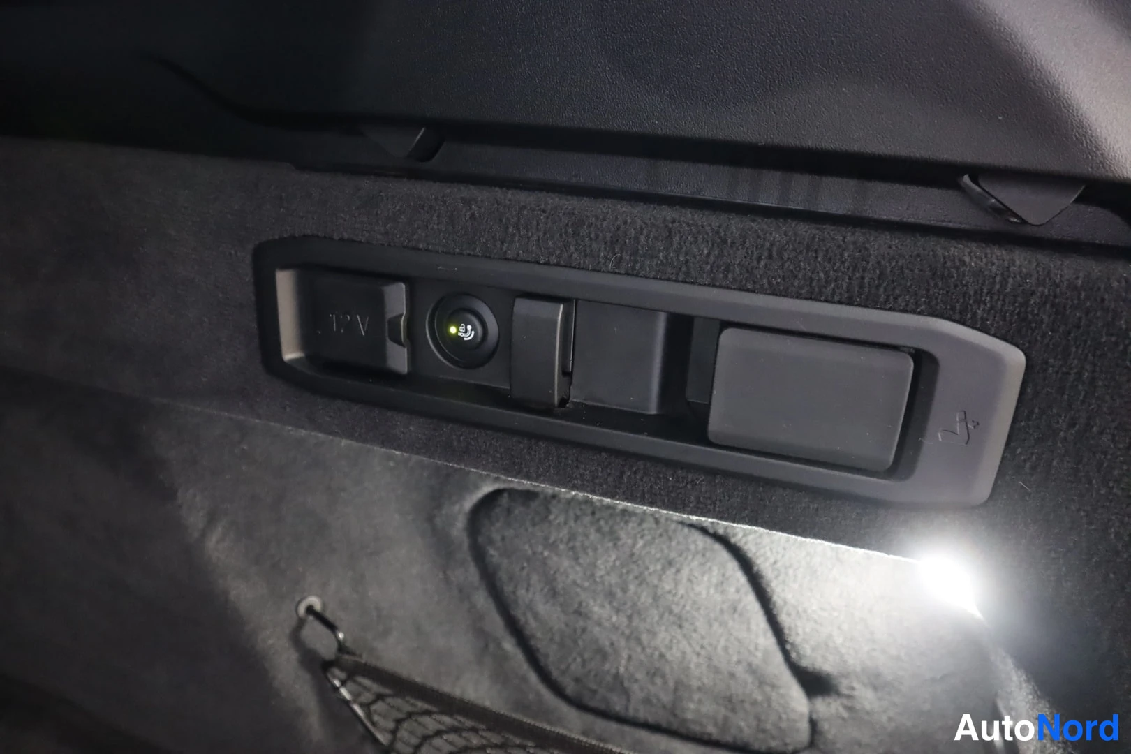 Muu: Tavaratilan sisäpanelin sähkökäynnistyspainike ja 12 V-pistorasia mustassa verhouksessa.