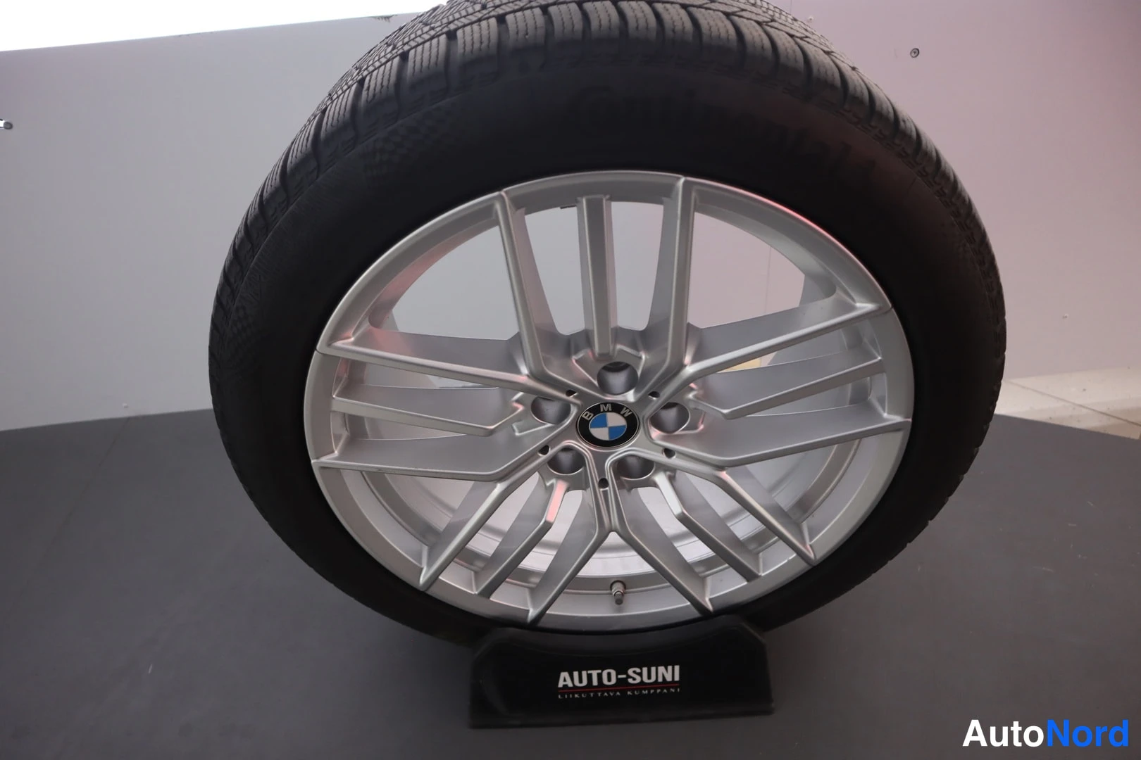 Muu: Erillinen lumirenkaan alloy-vanne, hopeinen BMW-merkinnällinen vanteen keskiö, näytteillä Auto-Suni-näytinvaihdossa.