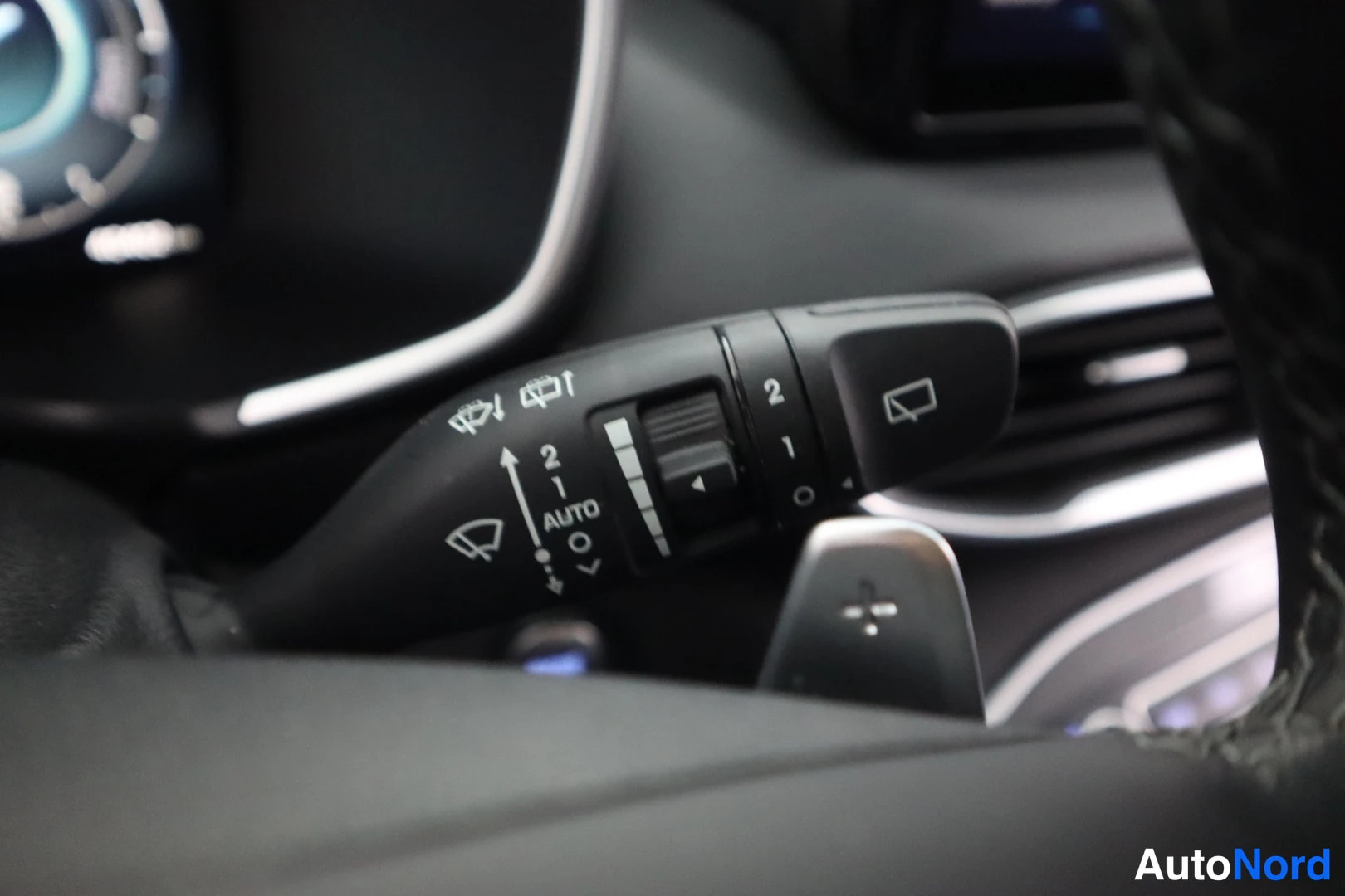 Yksityiskohta: Hyundai Santa Fe -henkilöauton pyyhkäisimien vipu AUTO- ja nopeusmerkinnöillä, taustalla kojelaudan viritelmät.