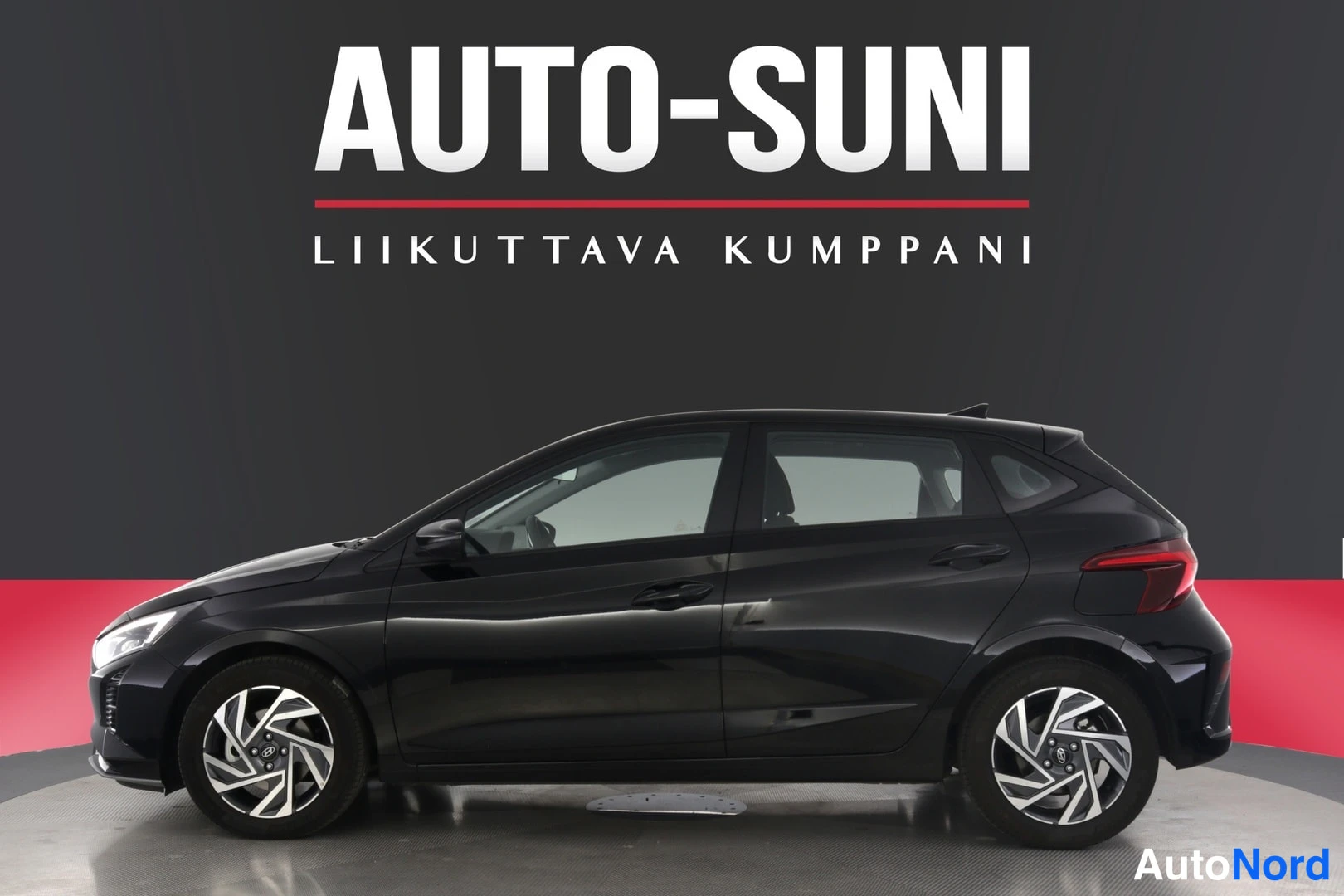 Sivulta: Auton sivuprofiili tummana, näkyvät ovet, pyörät ja takavalo myyntitaulua vasten.