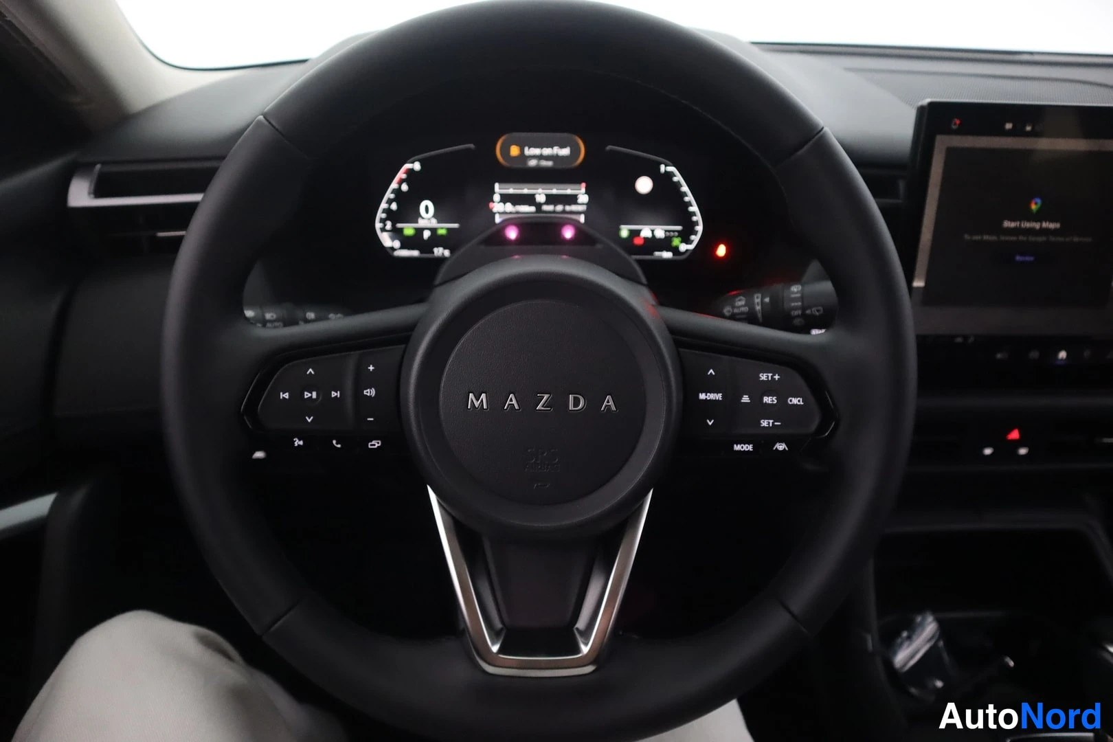 Muu: Mazdan ohjaamon etuosan näkymä: Mazda-merkkinen ohjauspyörä, digitaalinen mittaristo ja infotainment-näyttö, jossa lukee 'Start Using Maps'.
