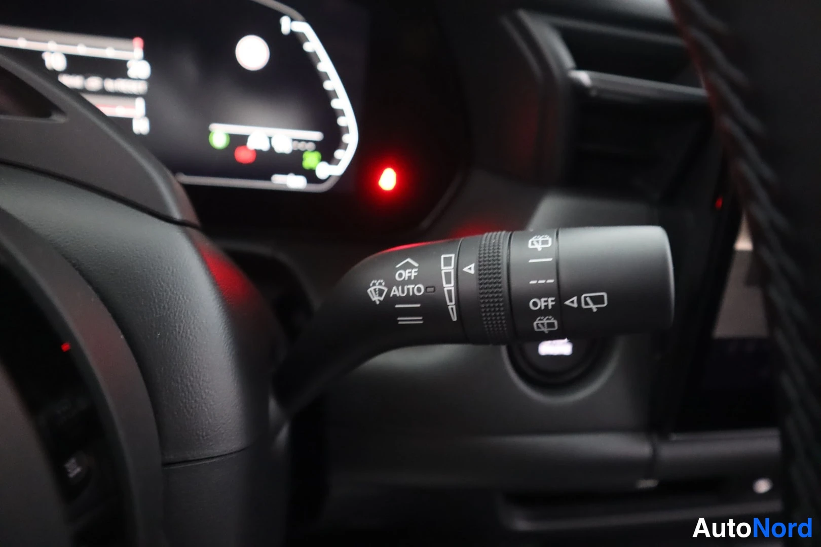 Yksityiskohta: Sisätilakuva: ohjauspyöränvarcharan vasen vipu tuulilasinpyyhkijöille, merkinnät OFF ja AUTO, takana osittain näkyvä digitaalinen mittaristo.