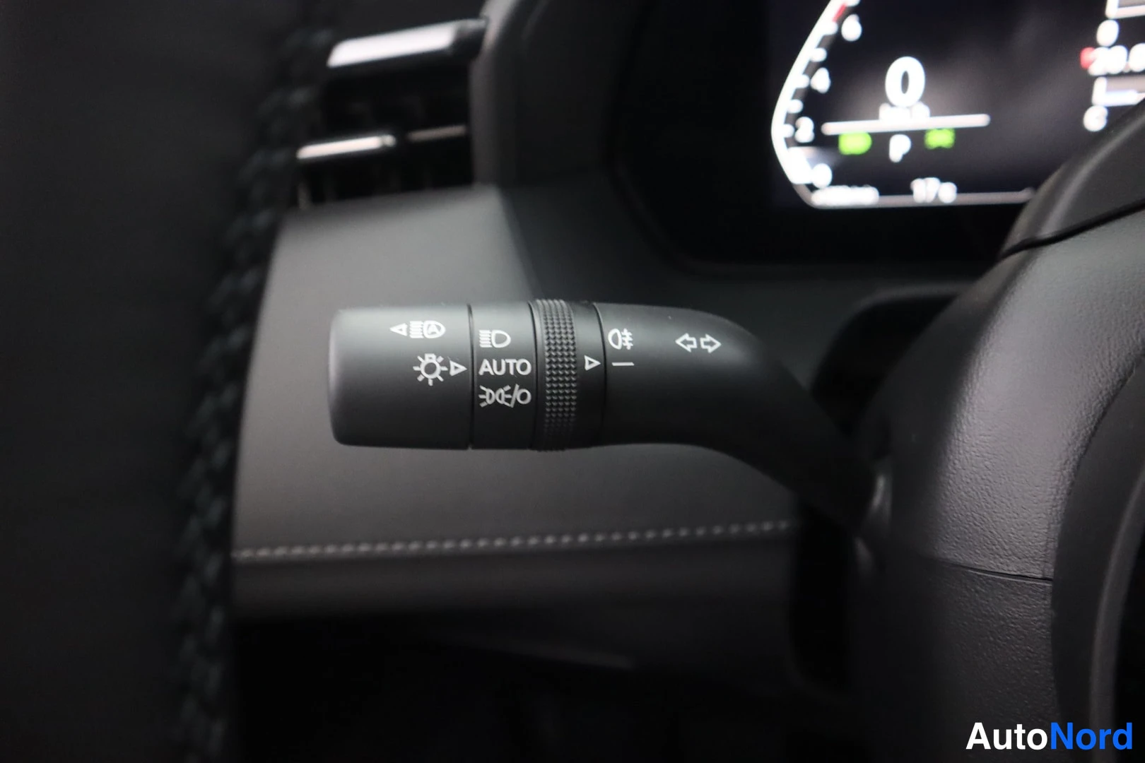 Yksityiskohta: Sisätilakuva: ohjauspyöränvarcharan vasen vipu valoille ja suuntavilkkuille, merkintä AUTO, taustalla digitaalinen mittaristo ja ilmastointisuuttimet.