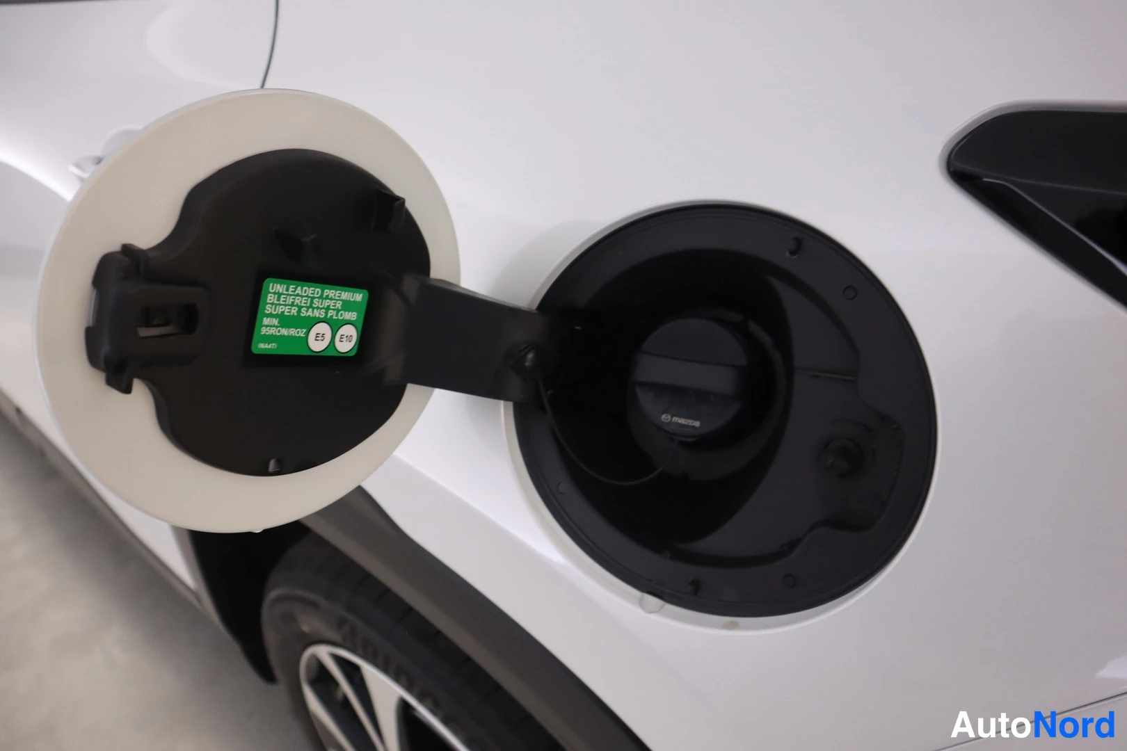 Muu: Avoin polttoainesäiliön luukku valkoisessa autonrunnossa; kannessa vihreä tarrateksti ja sisällä tumma tankin korkki.