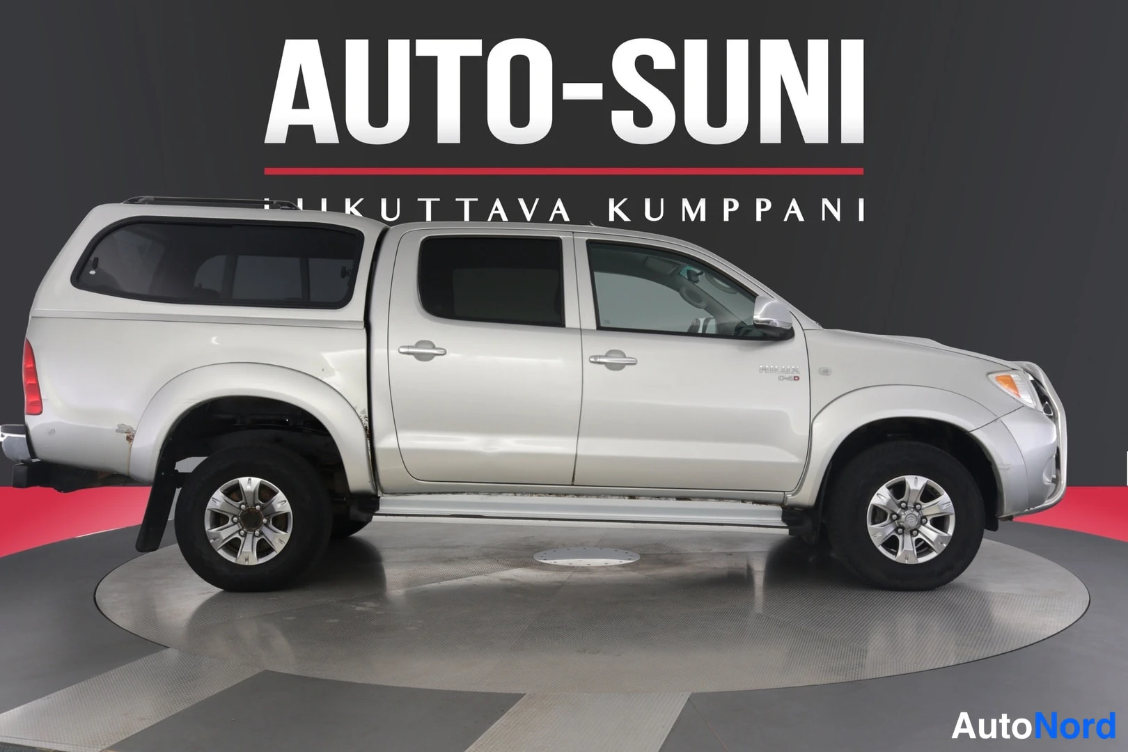 Sivulta: Hopea Toyota Hilux -lainen avolava-auto sivulta kuvattuna, lavalla kuomilisä, oviparien alla sivupolkimet.