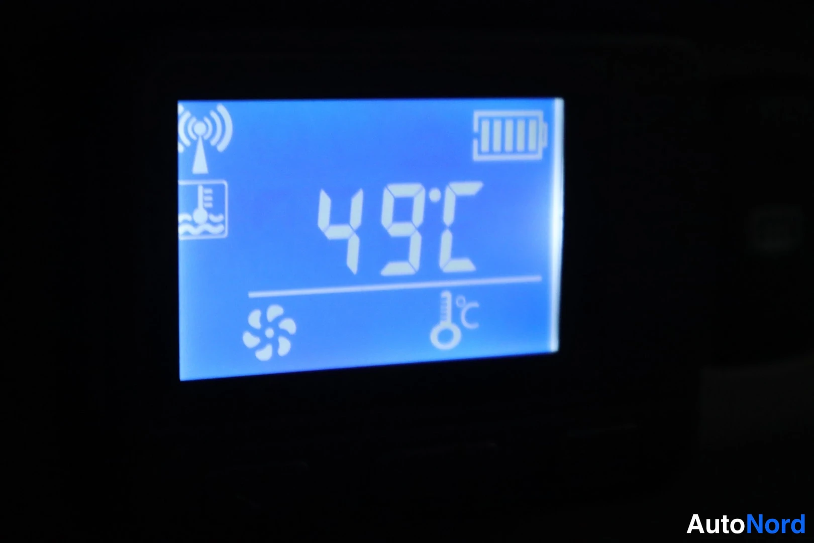Muu: Sinitaustainen ajoneuvon näyttö näyttää lämpötilan 49°C, kuvakkeina antenni, akku ja lämpömittari.