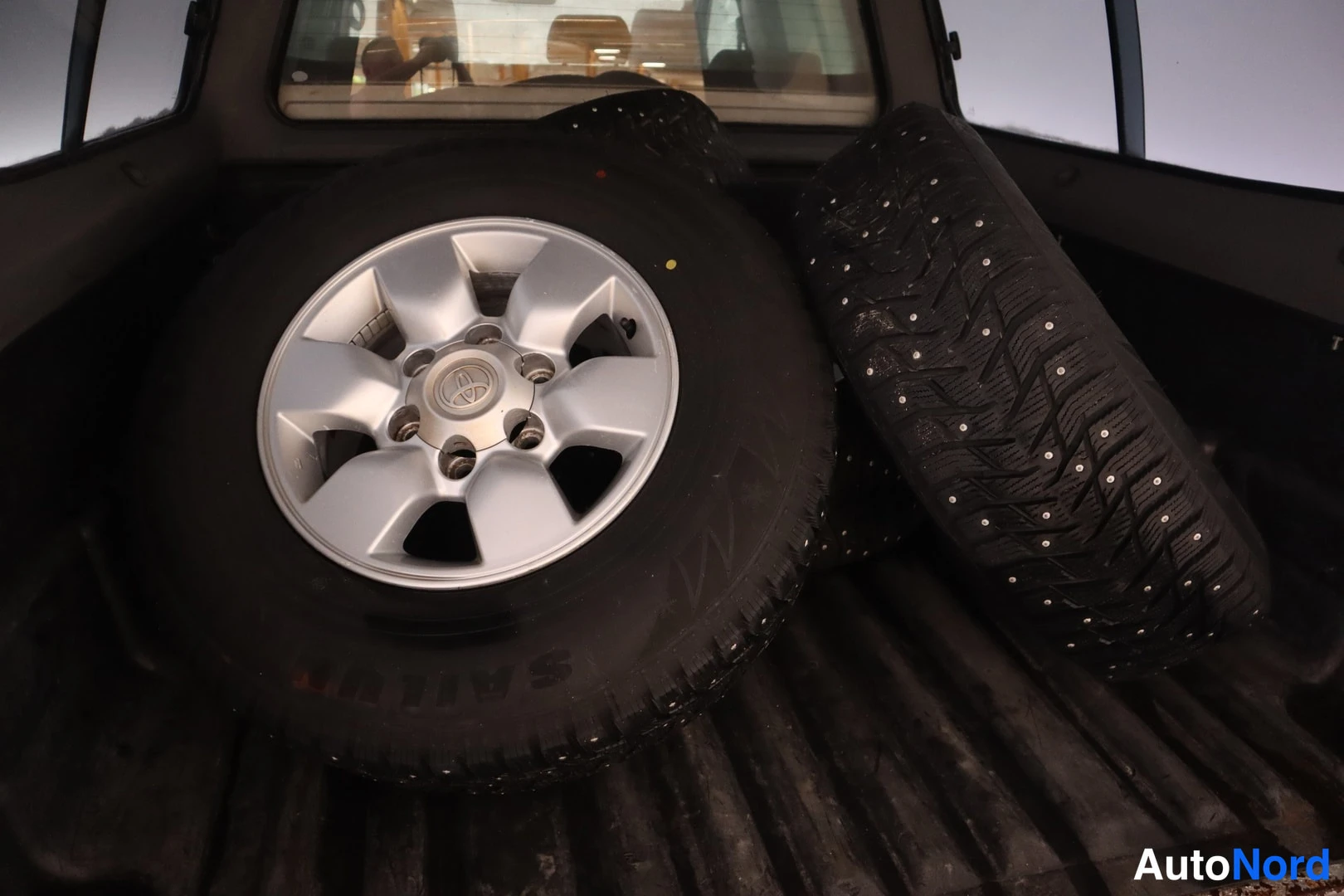 Takaa: Kolme nastarenkasta auton lavassa;Toyota-merkitty kettupyörä etualalla.