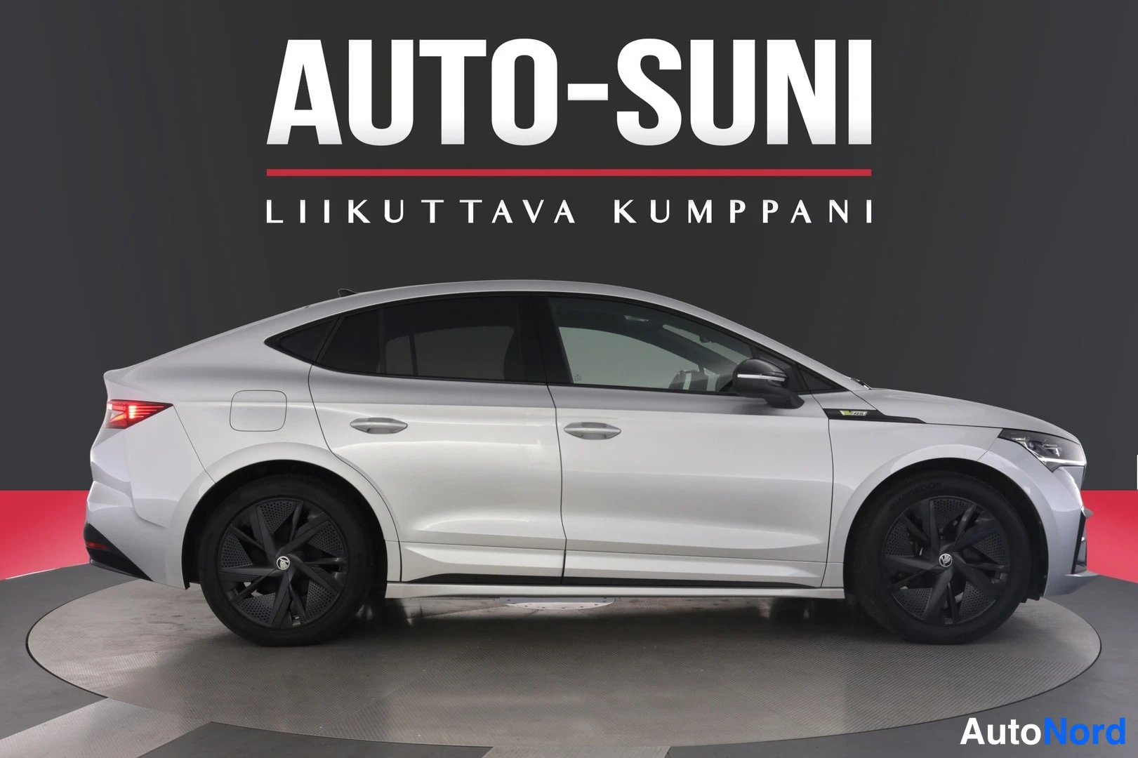 Etuviisto, nokka oikealle: Hopeanvärinen Skoda Enyaq vasen kylki viistosti etuosaan; ajovalo pilottuvat kuvan oikeassa reunassa, tummat kevytmetallivanteet.