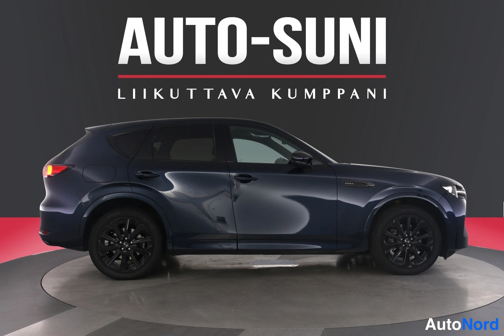 Etuviisto, nokka oikealle: Tummansininen farmarityyppinen henkilauto sivulta, keula oikealla; mustat vanteet ja tummat ikkunat.