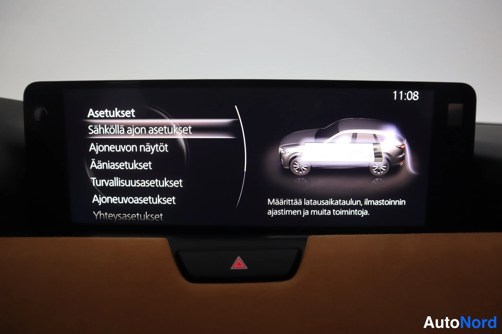 Yksityiskohta: Infotainment-näytön asetusvalikko 'Asetukset' ja 'Sähköllä ajon asetukset' valittuna, oikealla auton kuva ja teksti latausaikataulusta.