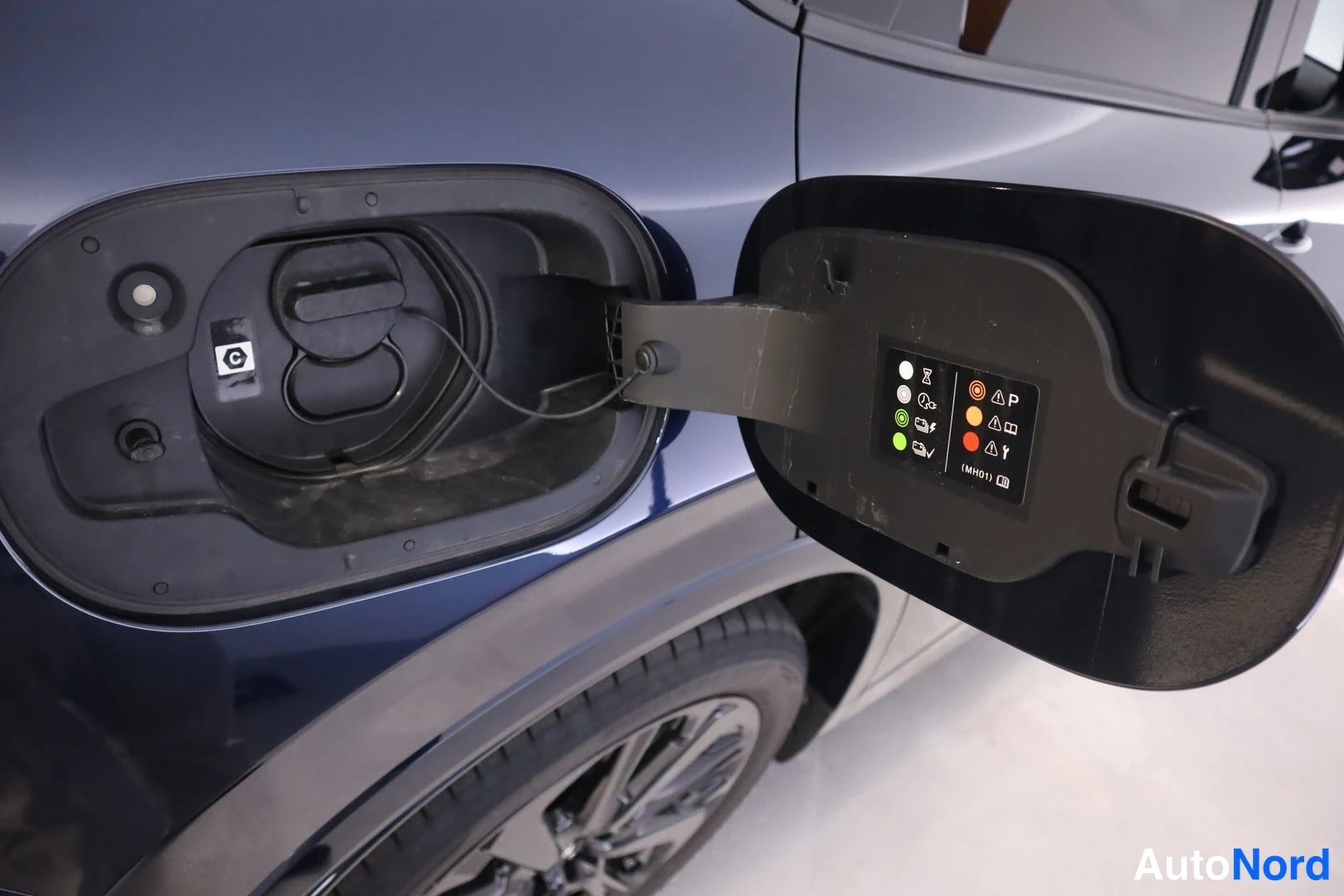 Sivulta: Avoimessa polttoainetäyttöluukussa näkyy tankin suljin ja varoitusmerkintätarra, autossa tummansininen koripaneeli.
