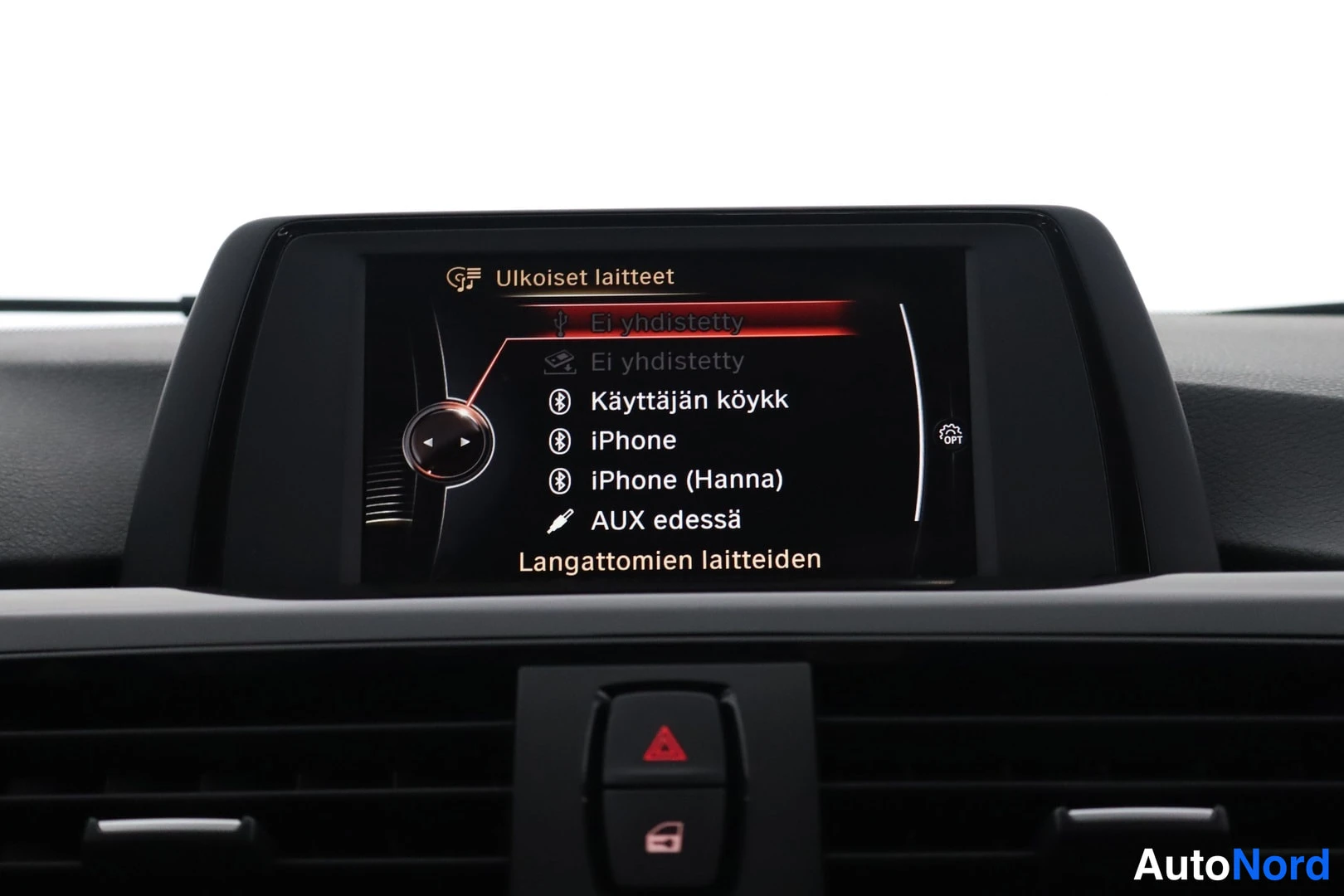 Yksityiskohta: Infotainment-näytön Ulkoiset laitteet -valikko listaa Ei yhdistetty, Käyttäjän köykk, iPhone, iPhone (Hanna) ja AUX edessä.