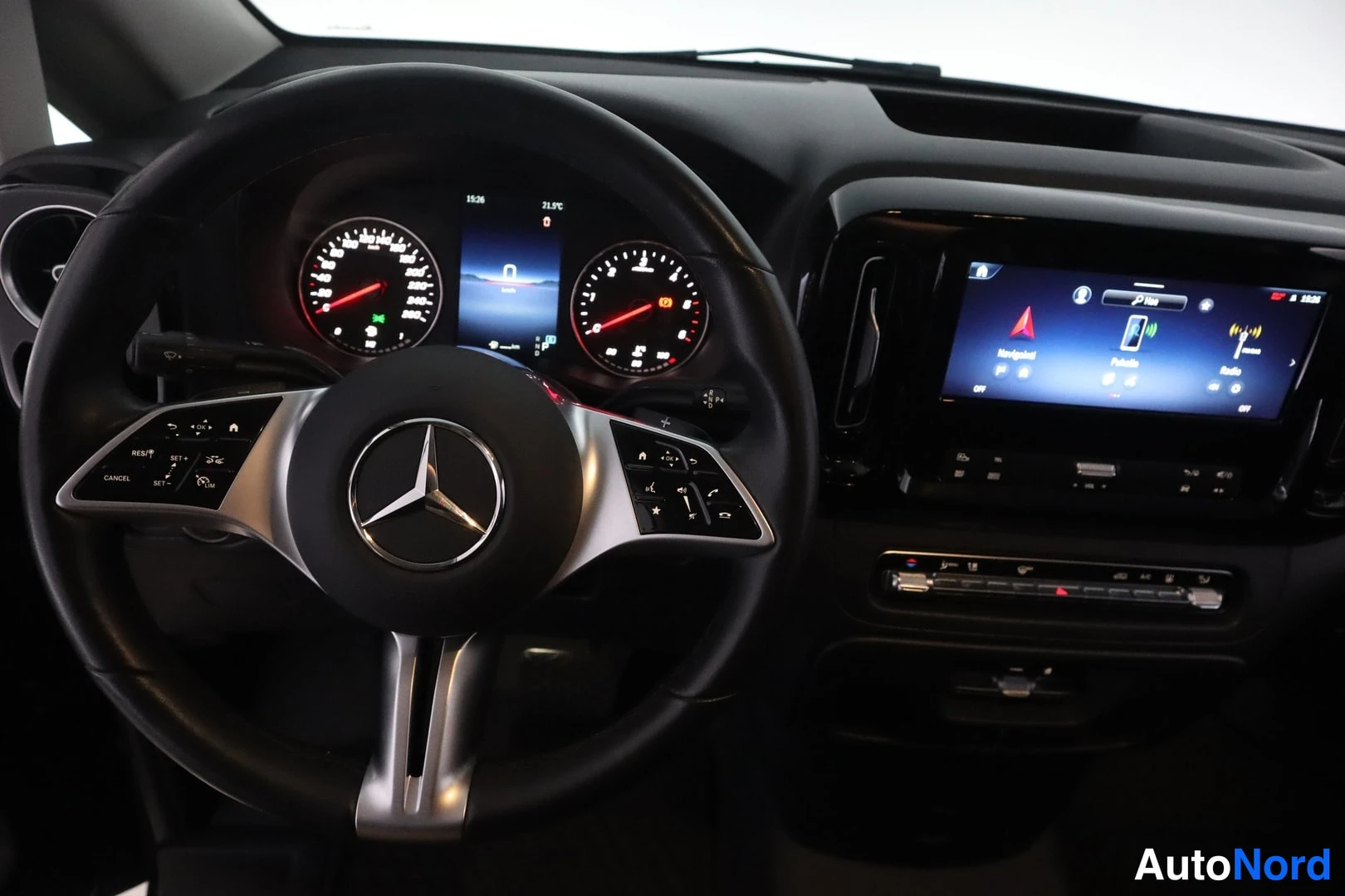 Muu: Kuljettajan näkymä Mercedes-Benzin ohjaamossa: monitoimiohjauspyörä Mercedes-tähtimerkillä, digitaalinen mittaristo (15:26, 21.9°C), keskusnäyttö navigointi-, p