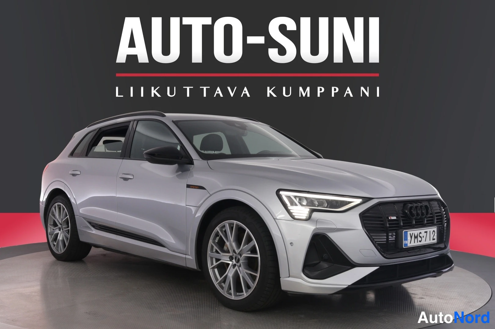 Etuviisto, nokka oikealle: Audi e-tron -maasturin etukulmanäyttö, autossa on vaalea hopeanvärinen maalipinta, musta etusäleikkö ja kevytmetallivanteet.